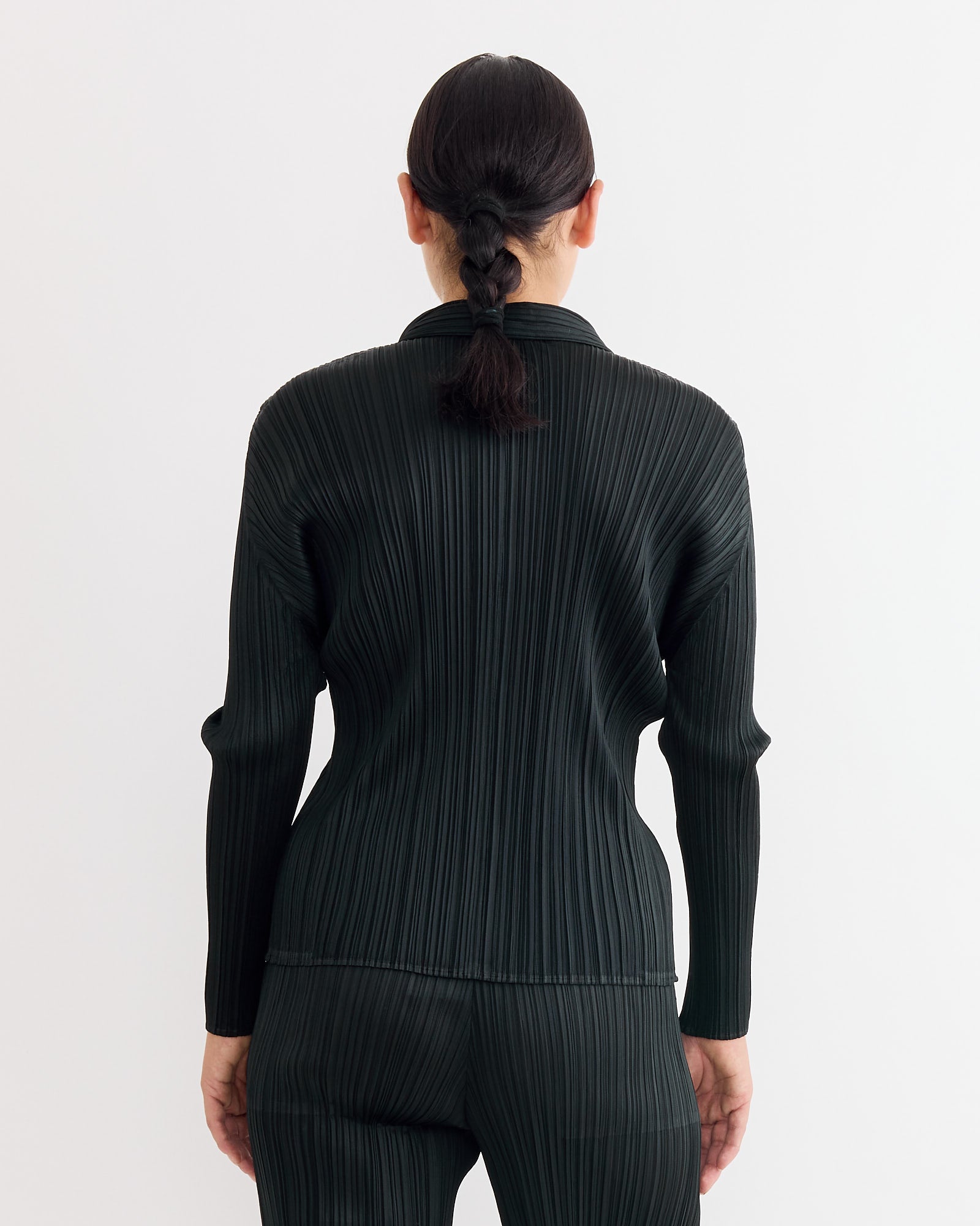A person with dark braided hair, seen from behind against a white background, wears the Pleats Please Issey Miyake Basics Shirt in Black.