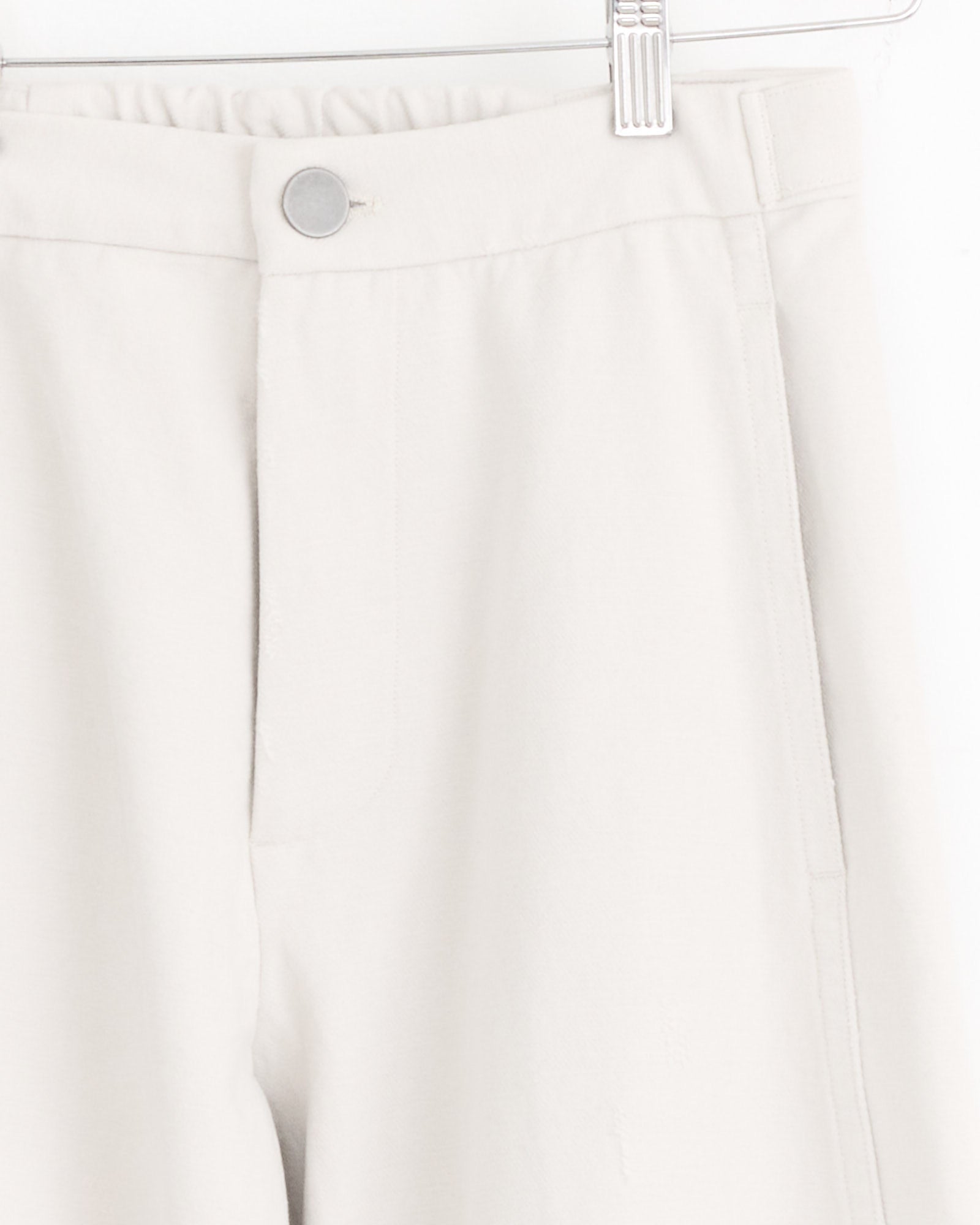 Close-up of the Lauren Manoogian Worn Pant in Worn Chalk, hanging on a hanger, highlighting the waistband with a silver button, belt loops, and side pockets. The 100% cotton fabric looks soft and slightly textured.