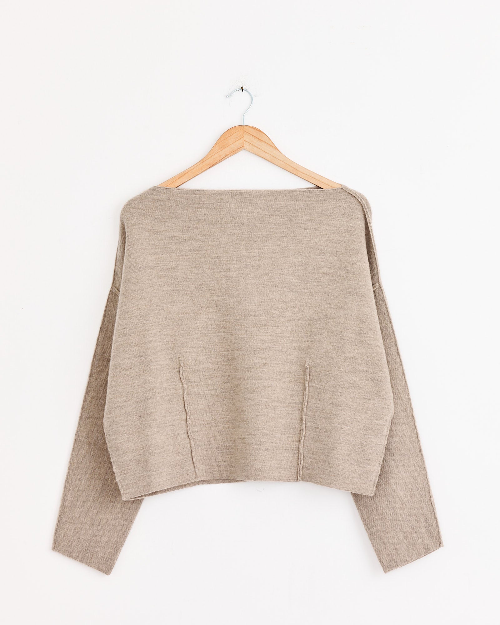 The Lauren Manoogian Double Knit Boatneck in Oak, a beige long-sleeved sweater, hangs on a wooden hanger against a plain white wall.