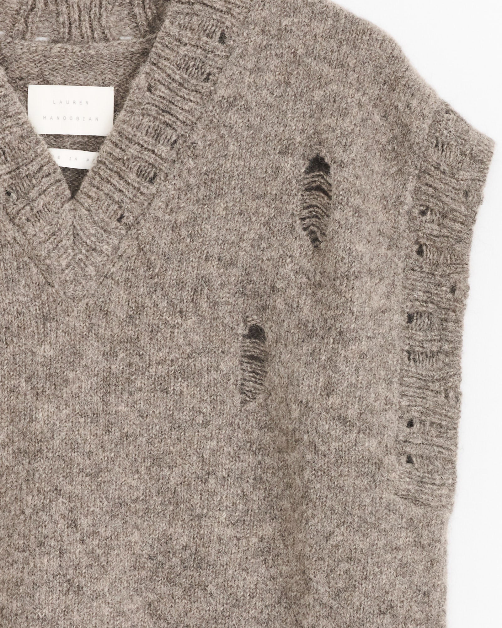 A close-up of the Lauren Manoogian Distressed Vest in Rock shows intentional distressed holes, a ribbed V-neck collar, and a partially visible fabric label inside the neckline.