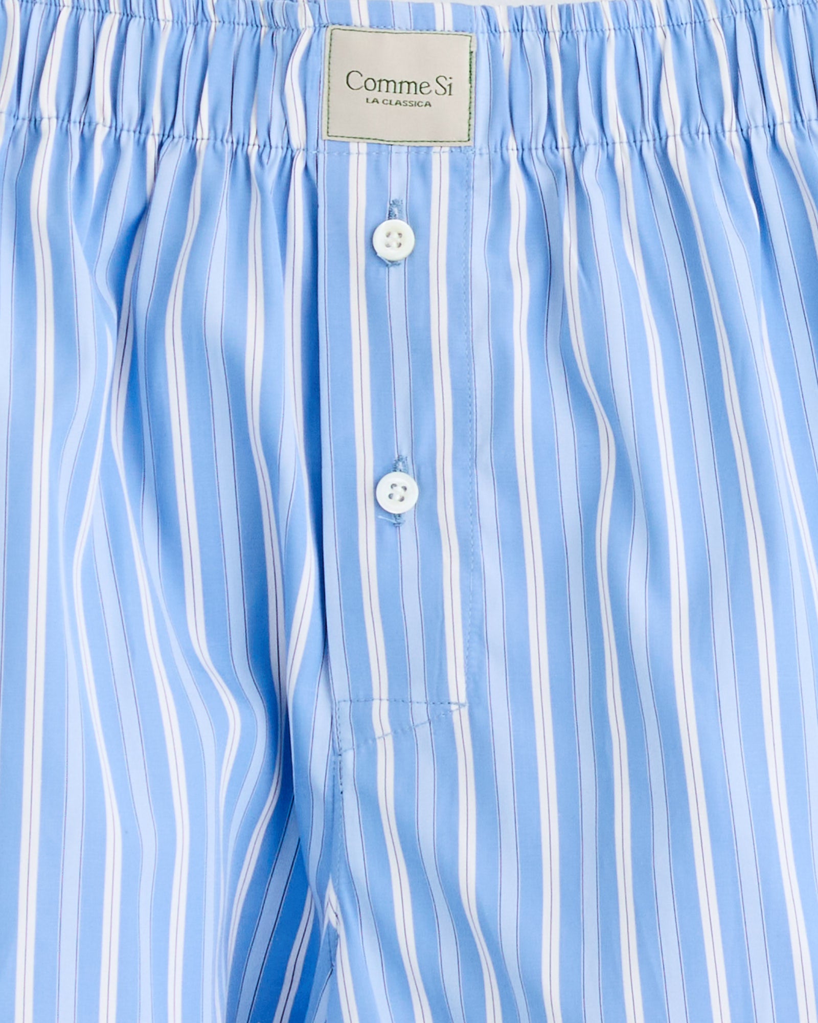 Close-up of Comme Si La Boxer Classica in Executive Stripe: light blue and white vertical stripes, elastic waistband, two white buttons, and LA CLASSICA label. Questions about fit or sizing? Chat with us online.