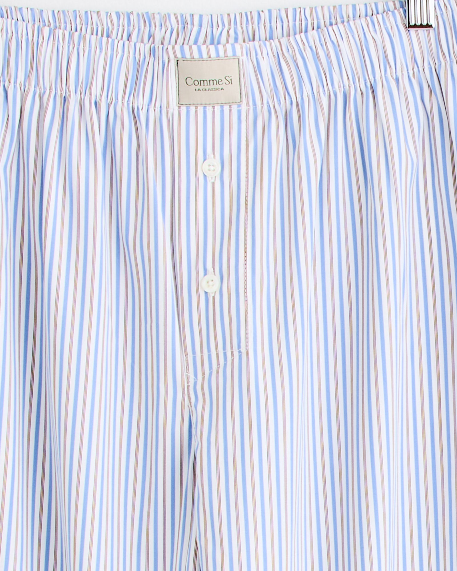 Close-up of the Comme Si La Boxer Alta in Ledger Stripe: light blue, white, and brown vertical stripes, elastic waistband, two buttons, and a branded label at the center. For fit questions, our online chat is here to help.
