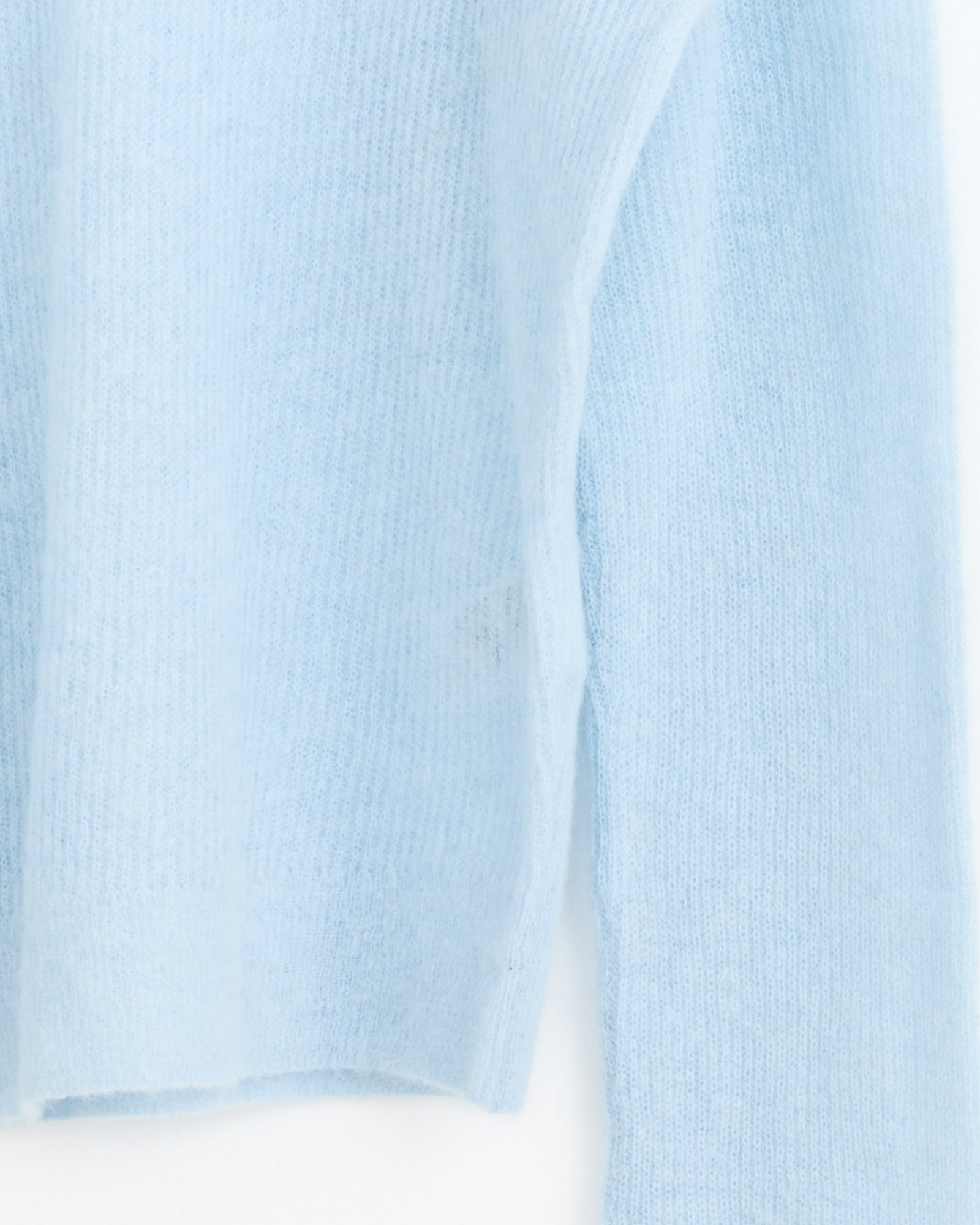 Close-up of the Auralee Baby Suri Alpaca Pullover in Light Blue, featuring a soft, fuzzy knit with ribbed texture on the torso and sleeve, showcasing this luxury sweater’s cozy and warm feel against a white background.