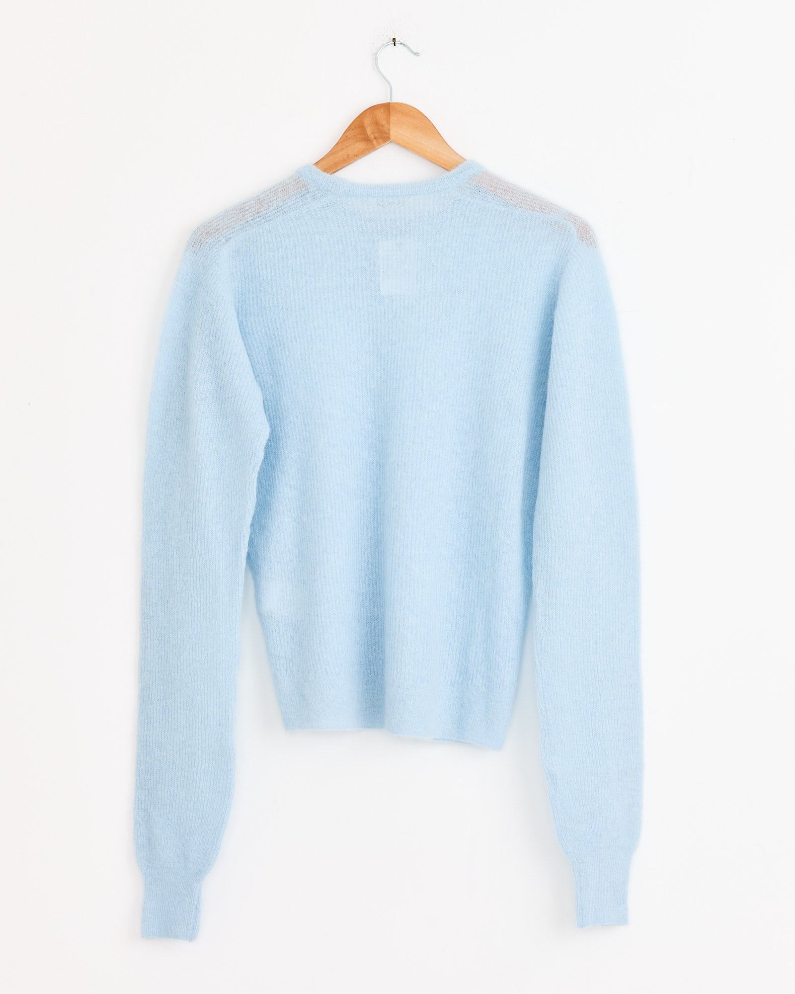 The Auralee Baby Suri Alpaca Pullover in Light Blue, a luxury long-sleeve knit, is displayed from the back on a wooden hanger against a white background.