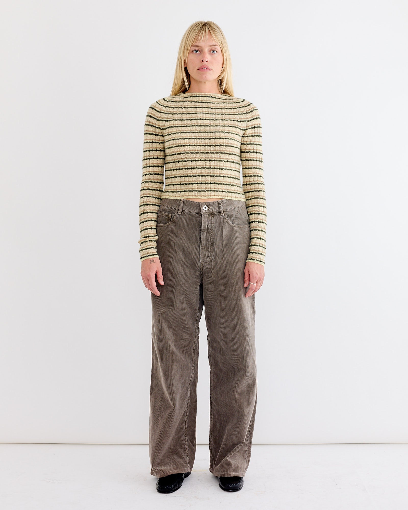 A woman with straight blonde hair wears the Auralee Wool Cashmere Boat Neck Pullover in Beige Stripe, standing facing forward against a plain white background.
