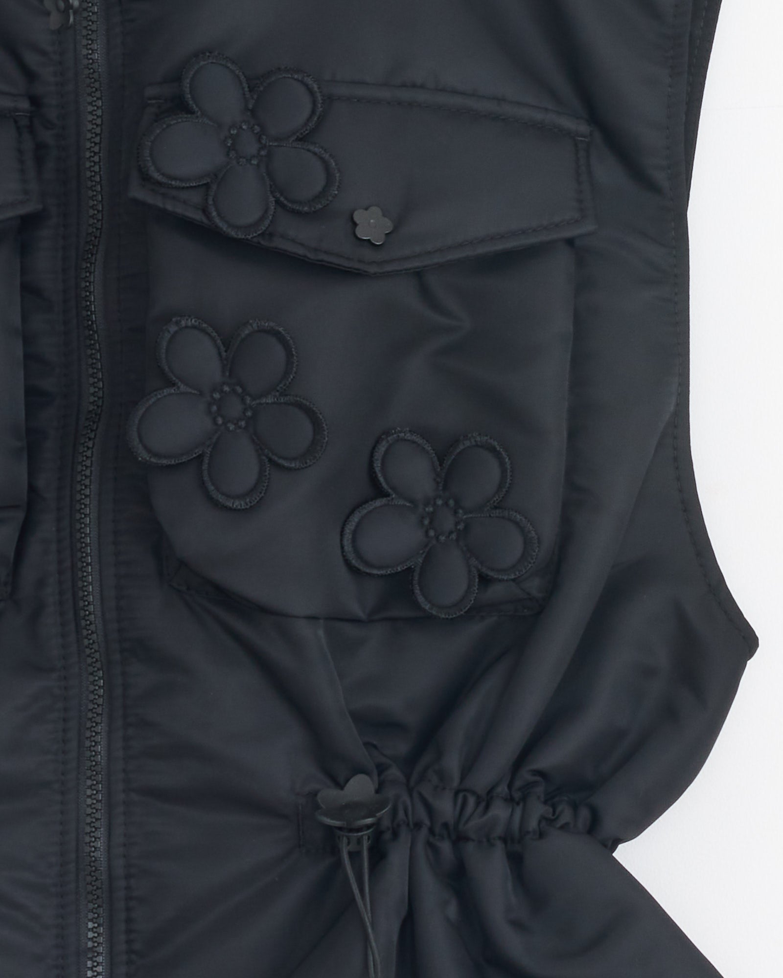 Close-up of the Bree Vest in Black by Cecilie Bahnsen, crafted from technical nylon with a zip-up front, gathered drawstring details, large flap pockets, and black flower appliqués.