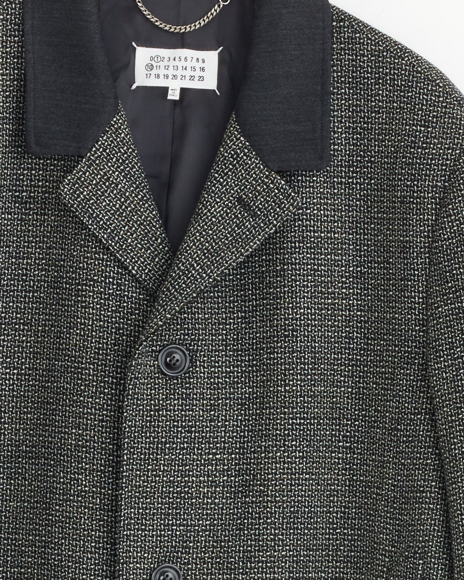 Close-up of a textured gray and black Maison Margiela Wool Coat in Grey with black lapels, two buttons, and a white tag showing numbers 0 to 23 inside the collar.