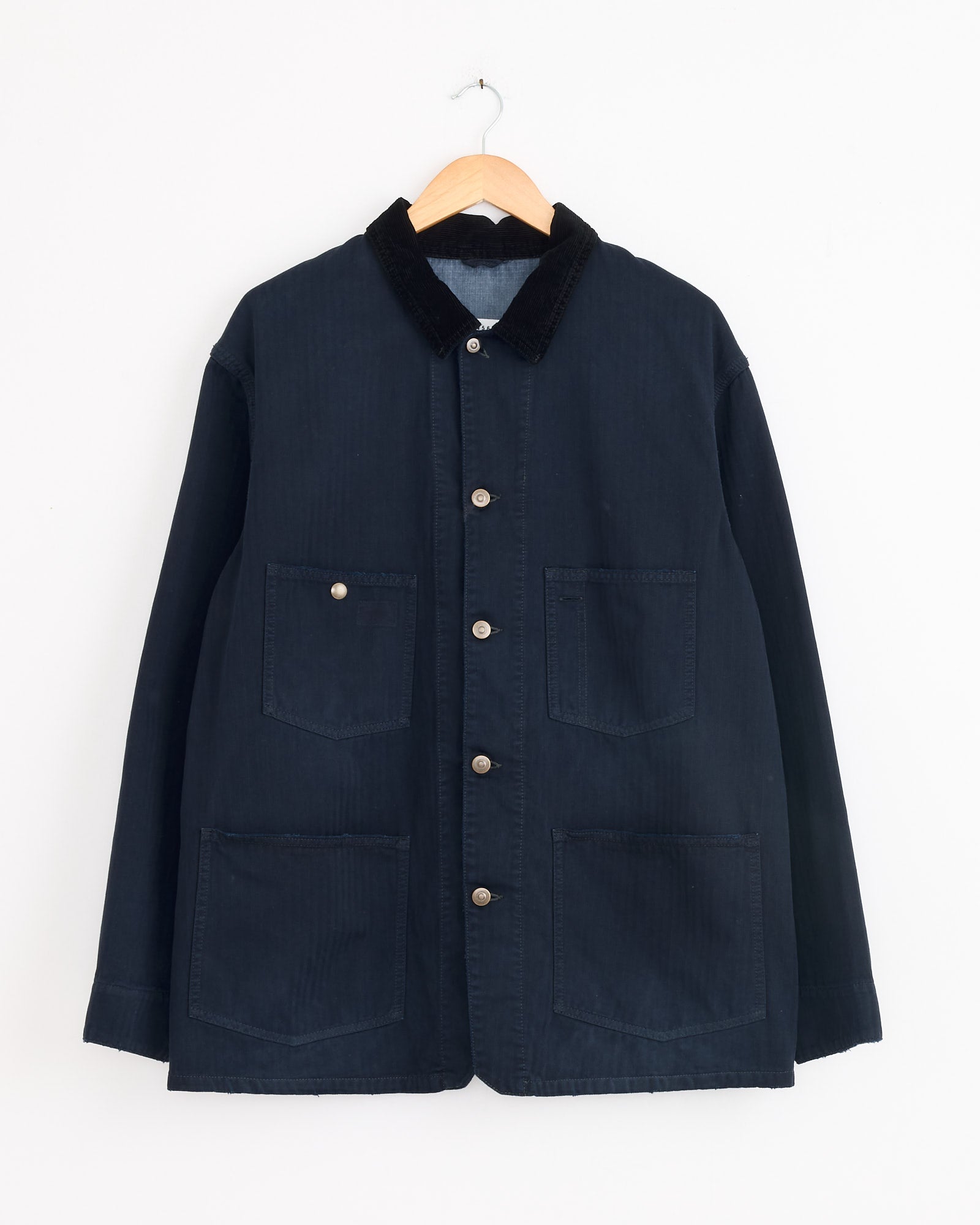 The Maison Margiela Sports Jacket in Dark Blue features a black corduroy collar, two chest pockets, and two large front pockets. Shown on a wooden hanger against a white background, this piece exemplifies timeless style.