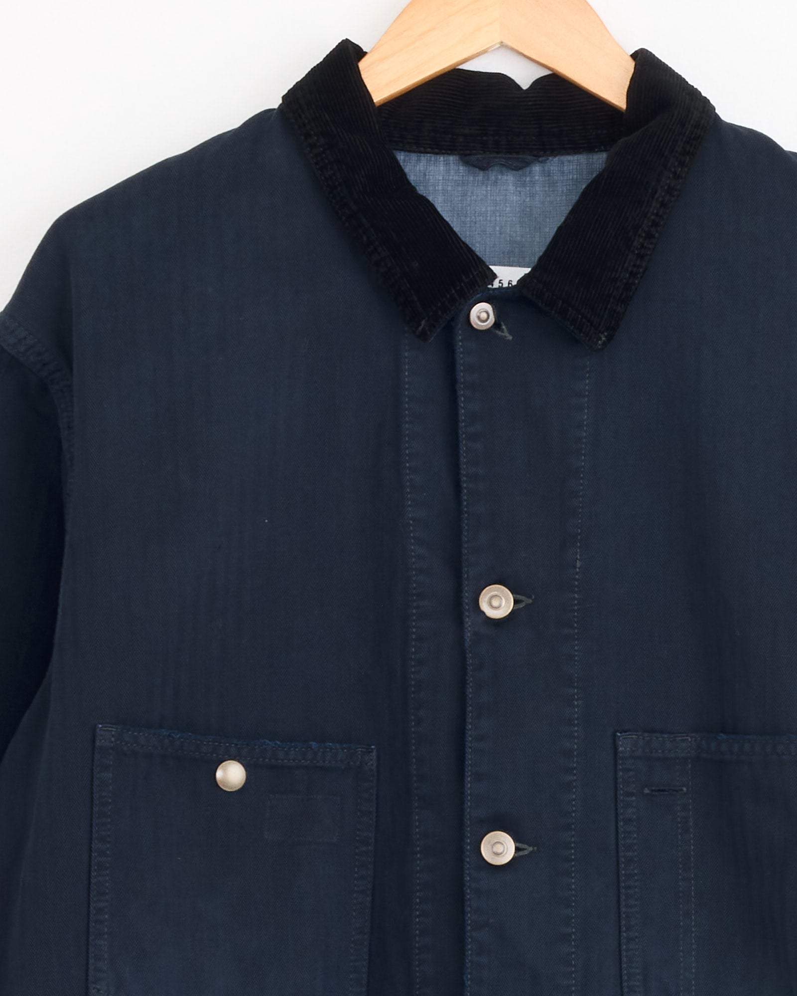 The Maison Margiela Sports Jacket in Dark Blue, featuring a black corduroy collar, beige buttons, and patch pockets, is displayed on a wooden hanger against a white background.