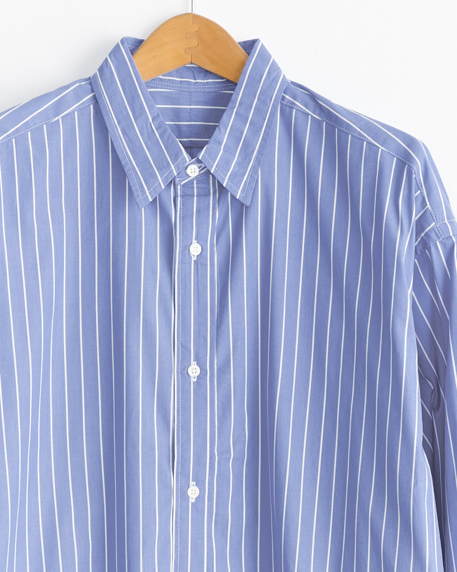 The Sillage Regular Wide High Count Shirt in White Stripe features blue and white vertical stripes and is displayed on a wooden hanger against a white background.