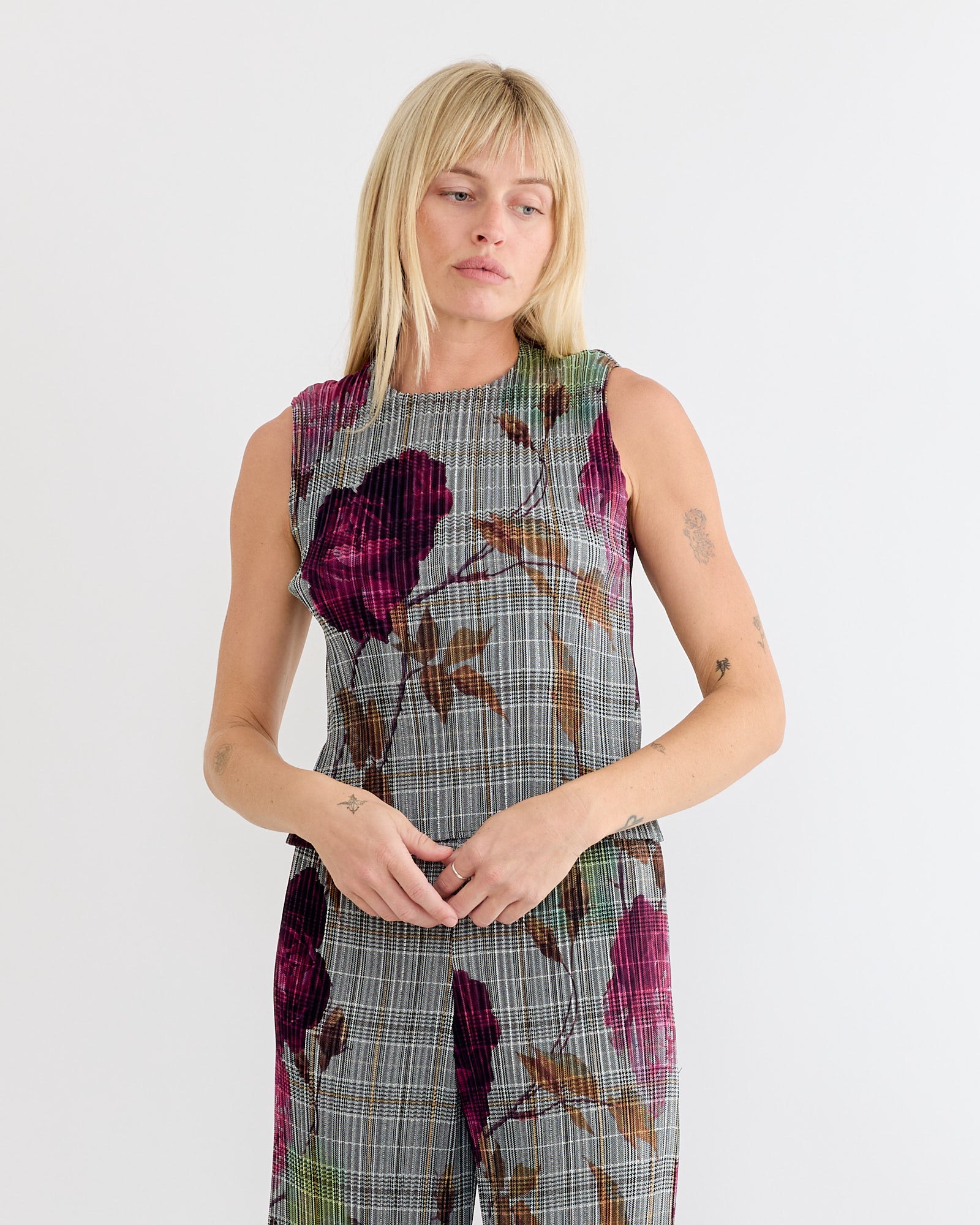 A blonde-haired person wears the sleeveless gray plaid Thelma Top in Rosalind by Julia Heuer and matching pants with a large purple Julia Heuer print, standing against a plain white background.