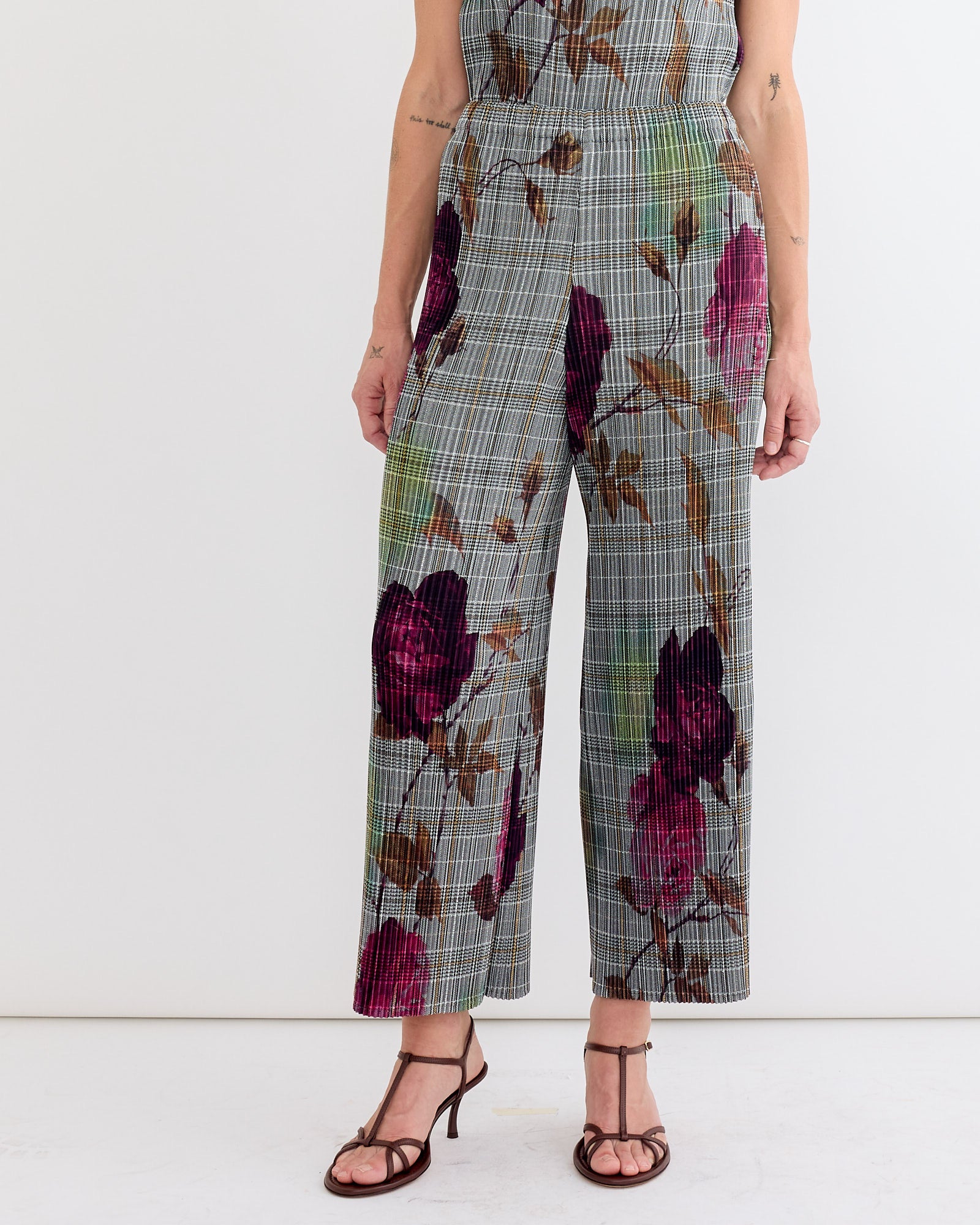 Someone wearing the Julia Heuer Jack Trouser in Rosalind—gray plaid wide-leg pants with pink and brown floral pattern—paired with dark strappy heeled sandals, stands against a plain white background.