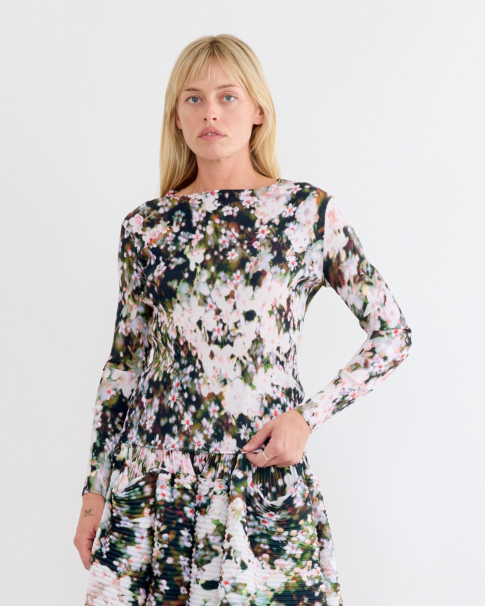 A woman with blonde hair wears the Julia Heuer Amy Top in Holle, which features a colorful, abstract floral pattern reminiscent of arashi shibori. She stands against a plain white background, looking at the camera with a neutral expression.