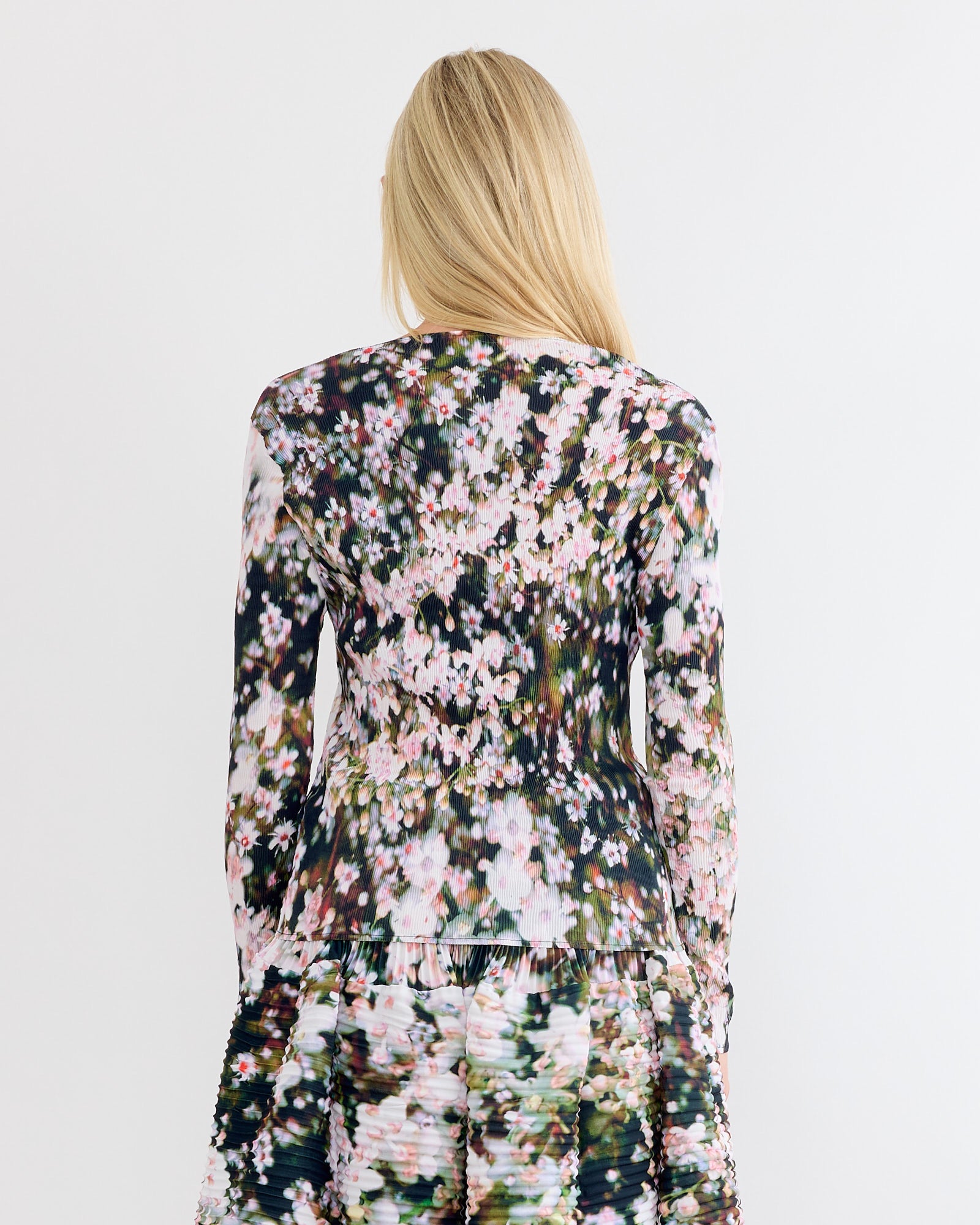 A person with long blonde hair, seen from the back, wears the Julia Heuer Amy Top in Holle with a matching skirt featuring a pink and green floral pattern, set against a plain white background.
