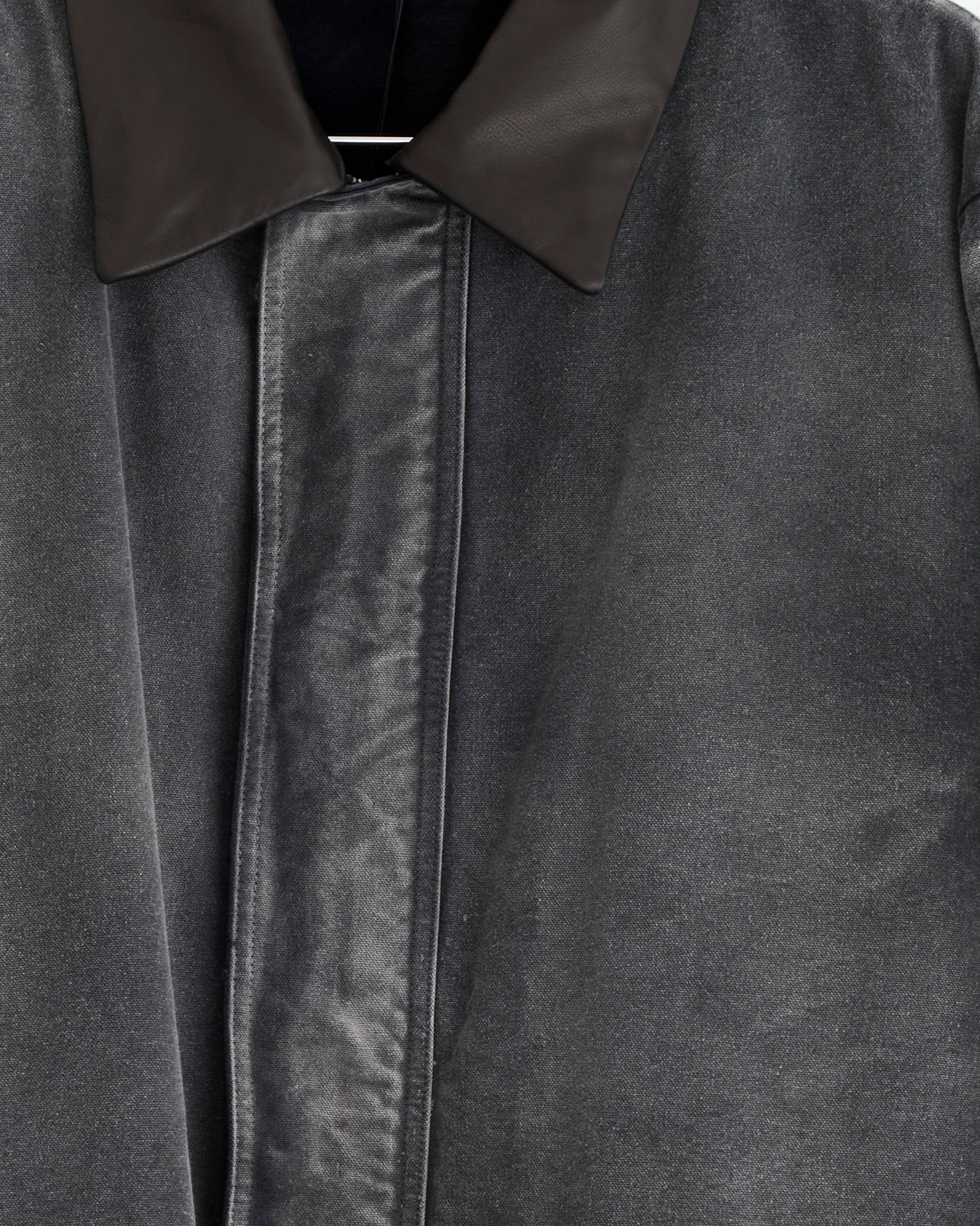 Close-up of the Auralee Dyed Duck Blouson in Faded Black, featuring dark grey textured fabric, a black leather collar, and concealed buttons reminiscent of vintage styles, with focus on the upper front.