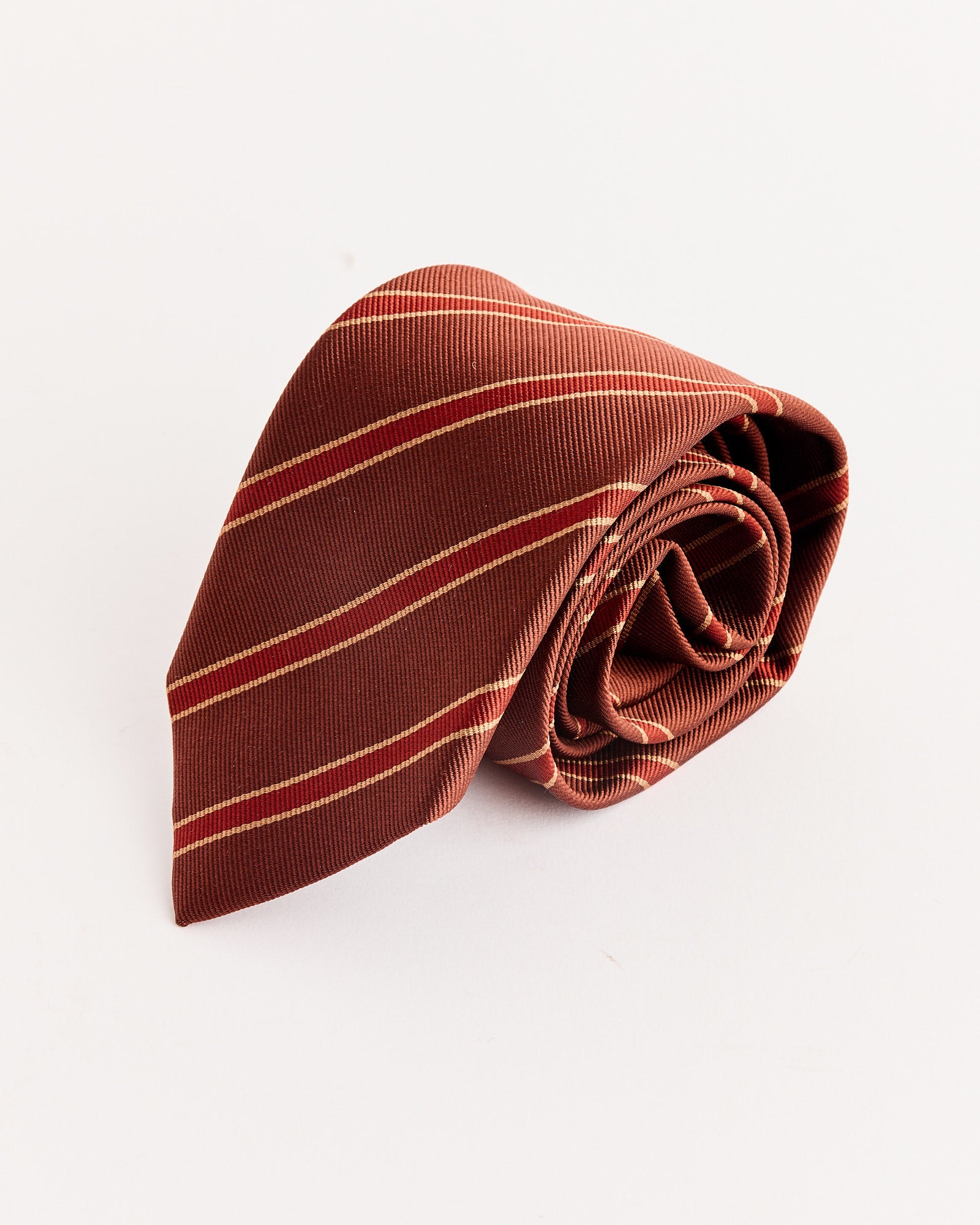 A Silk Stripe Tie in Burgundy by Auralee, crafted in Japan, is placed rolled up on a plain, light background.