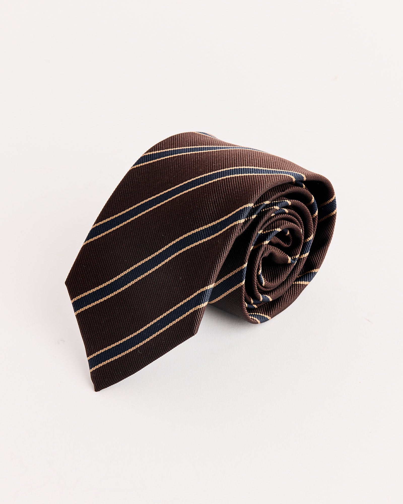 The Auralee Silk Stripe Tie in Dark Brown, made in Japan, features diagonal beige and blue stripes and is displayed on a plain white background.