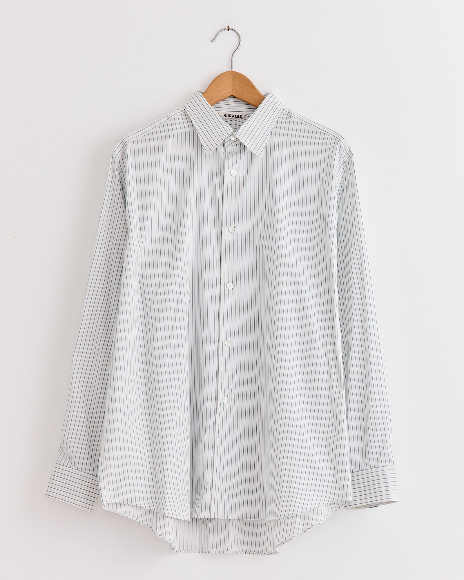 The Auralee Cotton Silk Stripe Shirt in White, crafted from premium Giza cotton, features black and white stripes and is displayed on a hanger.