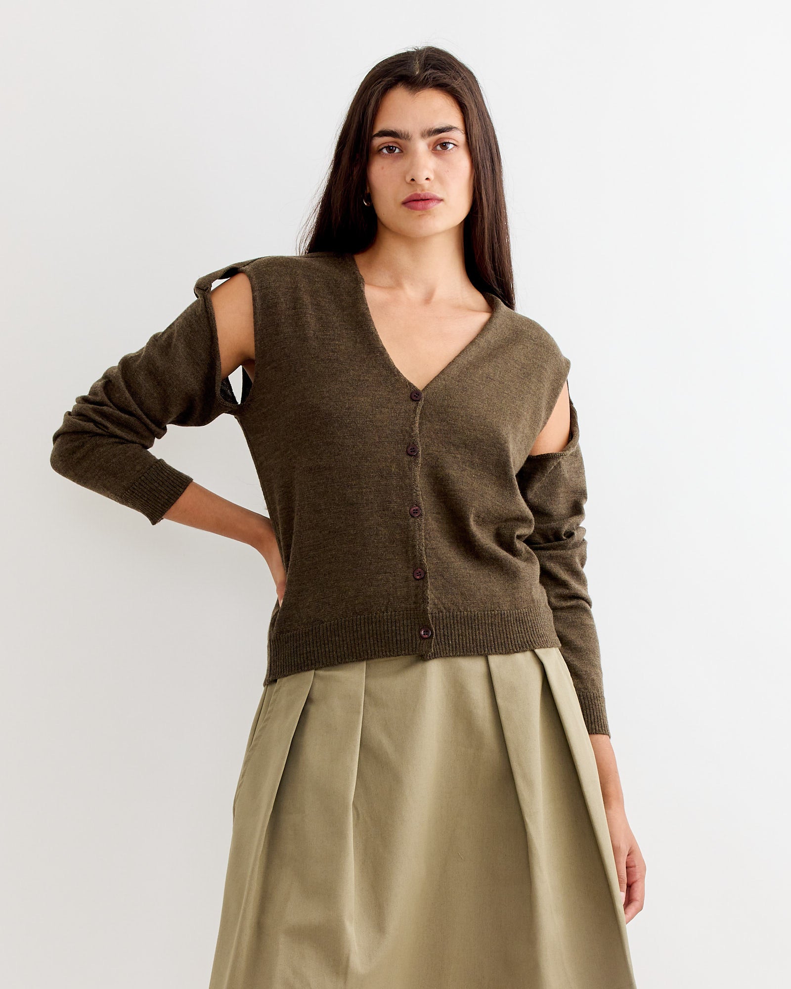 A woman with long dark hair wears the Gimaguas Coucou Cardigan in Brown with open shoulders and a matching skirt, posed against a plain white background with a neutral expression.