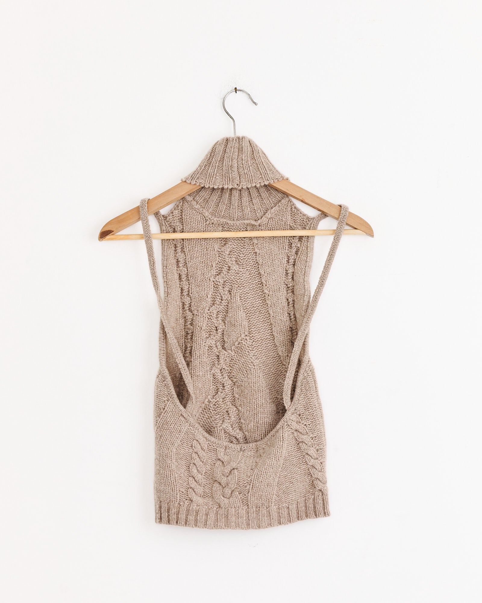 The Julita Top in Beige by Gimaguas, inspired by the original design, is a sleeveless extrafine wool knit vest with a cable pattern and exposed armholes, shown on a wooden hanger against a white background.