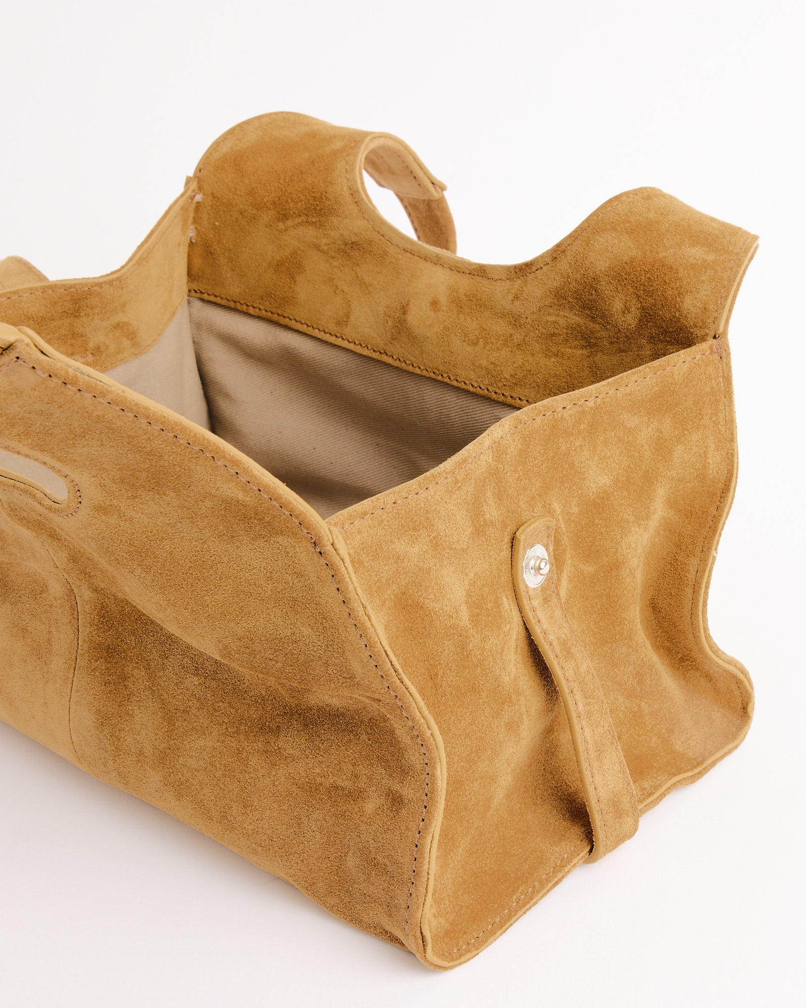The Mini Maria Suede Bag by Gimaguas is a tan shoulder bag with cutout handles, soft unstructured shape, beige fabric lining, and button snap closure—offering a relaxed, casual look ideal for everyday use.