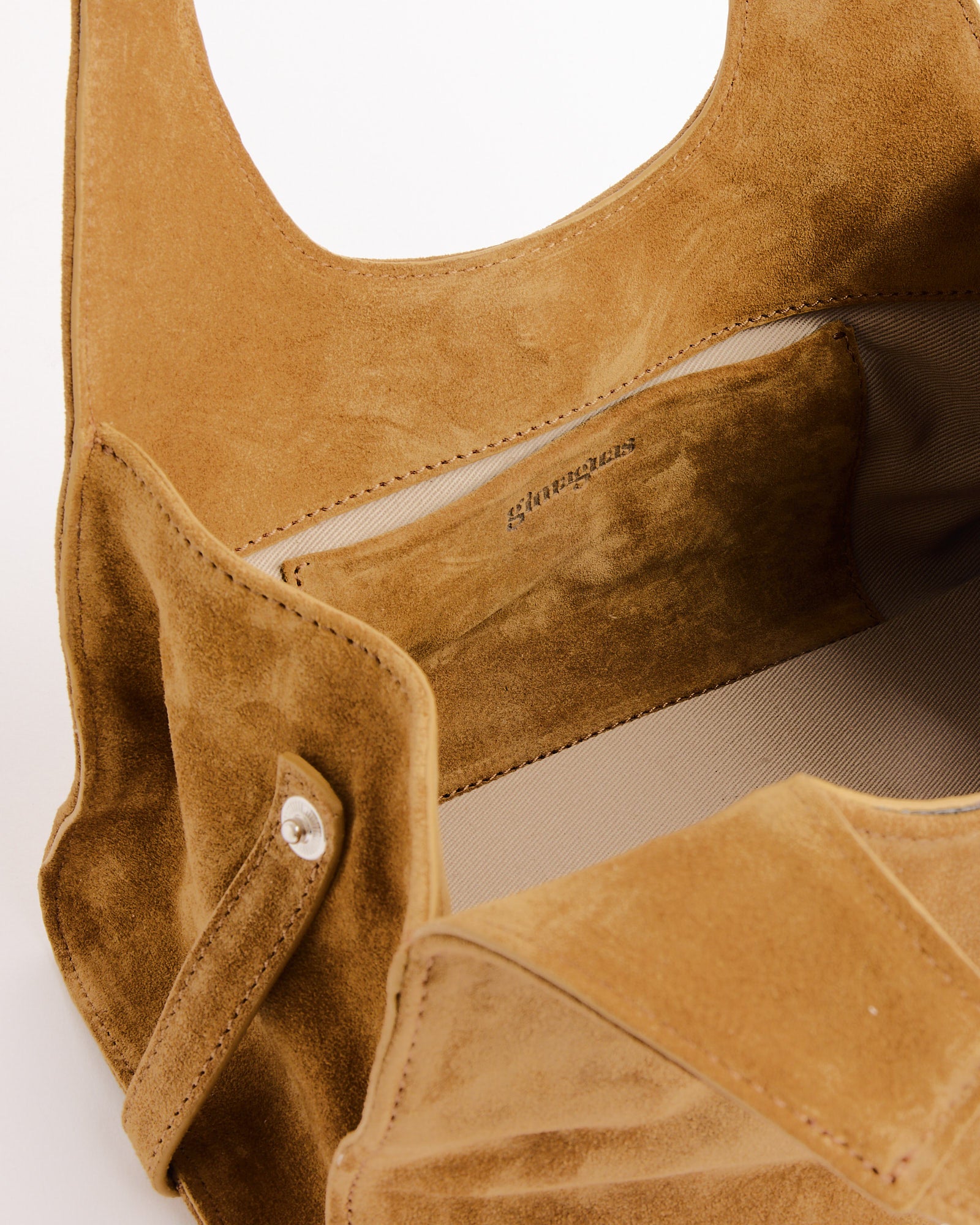 A close-up of an open tan Mini Maria Suede Bag by Gimaguas shows the interior pocket with a snap closure and fabric lining visible in this stylish shoulder bag.
