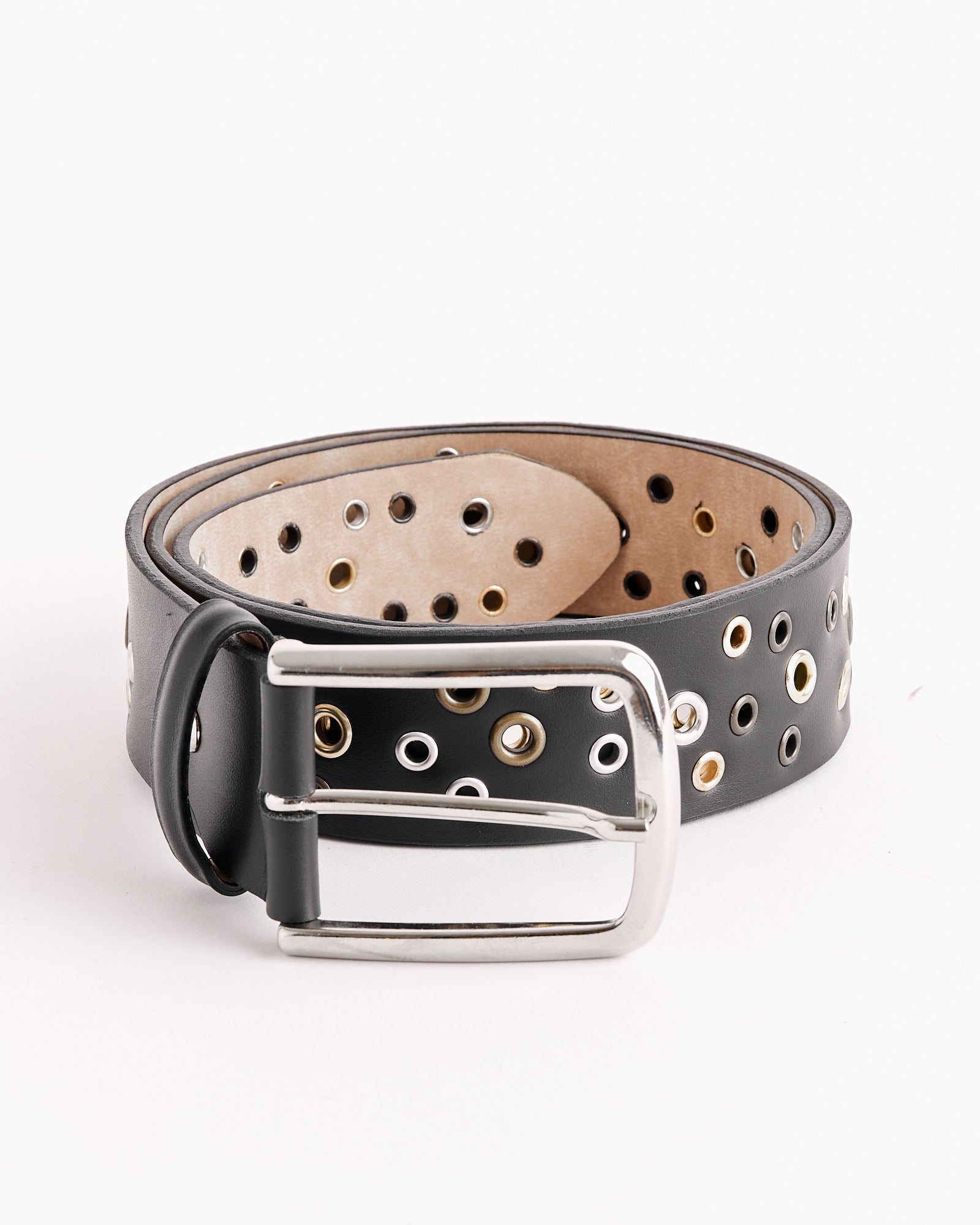 The Rufus Belt in Black by Gimaguas is a black leather belt with silver and gold grommet holes and a silver rectangular buckle, rolled up and shown on a white background. Find your perfect fit with our online chat support.