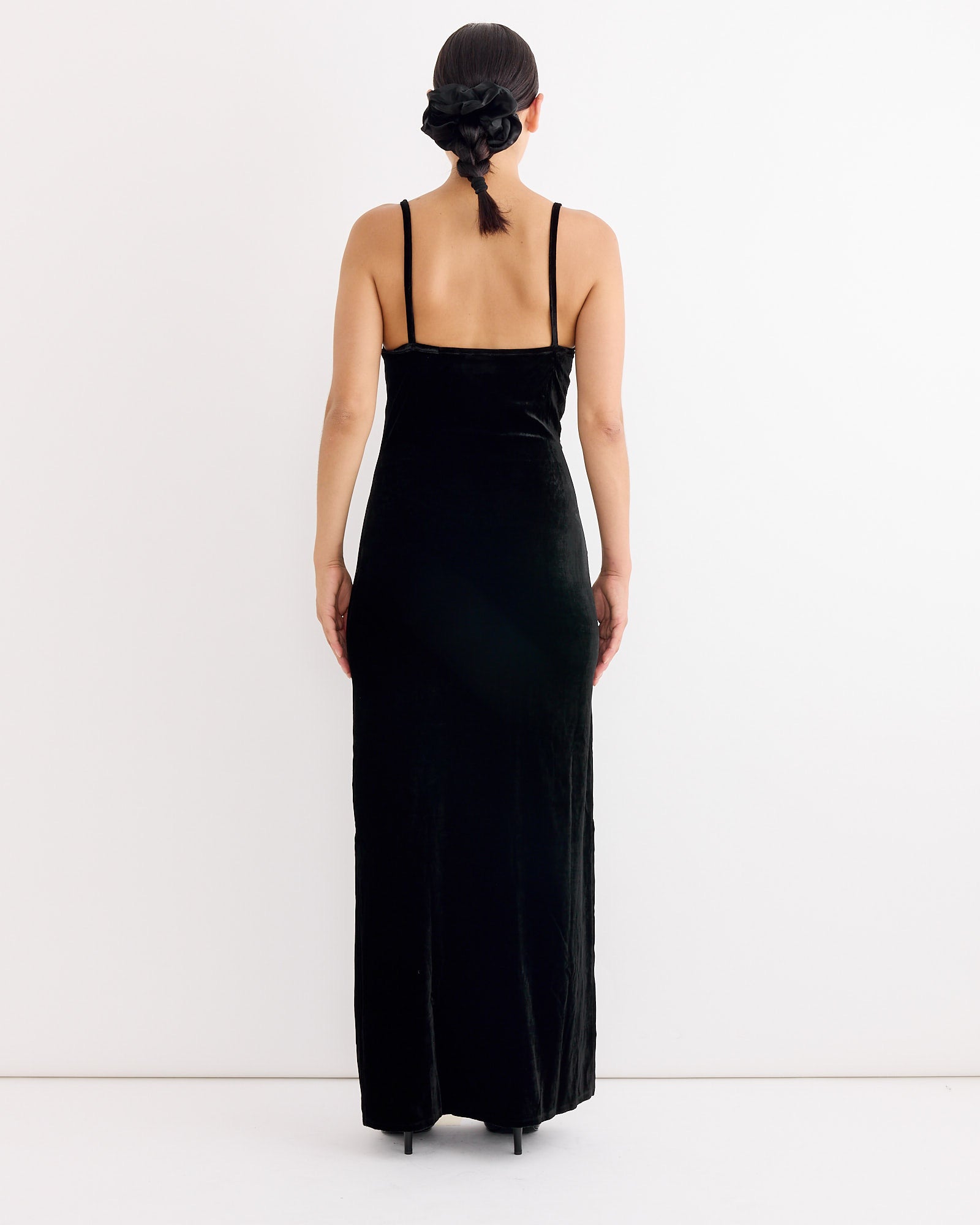 A person faces away from the camera, wearing Hai's Antoinette Dress in Black/Ivory with thin straps and black heels. Their dark hair is styled in a low bun, set against a plain white background.
