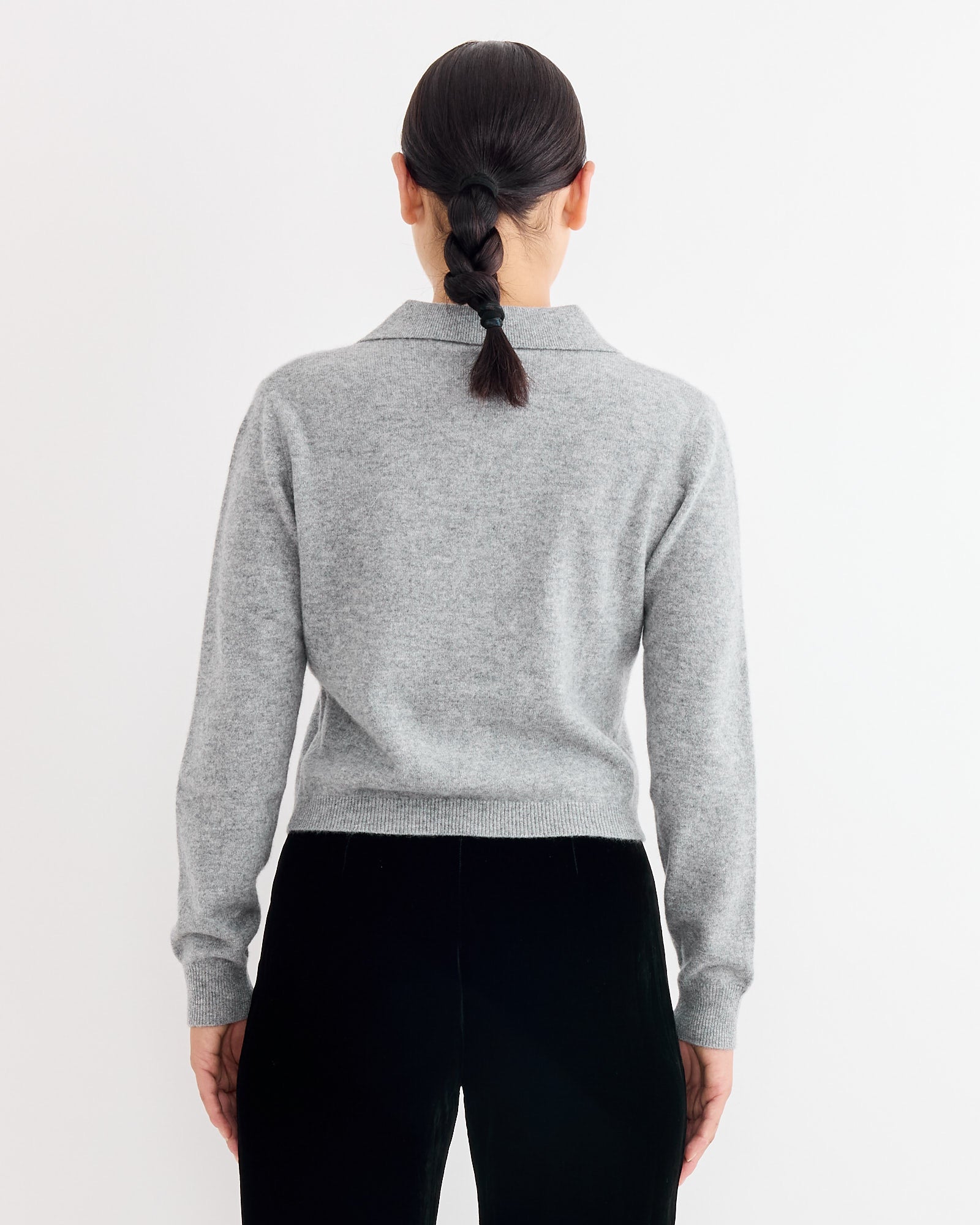 A person with dark hair in a single braid, wearing the Hai Anselma Cardigan in Grey and black pants, stands with their back to the camera against a plain white background.
