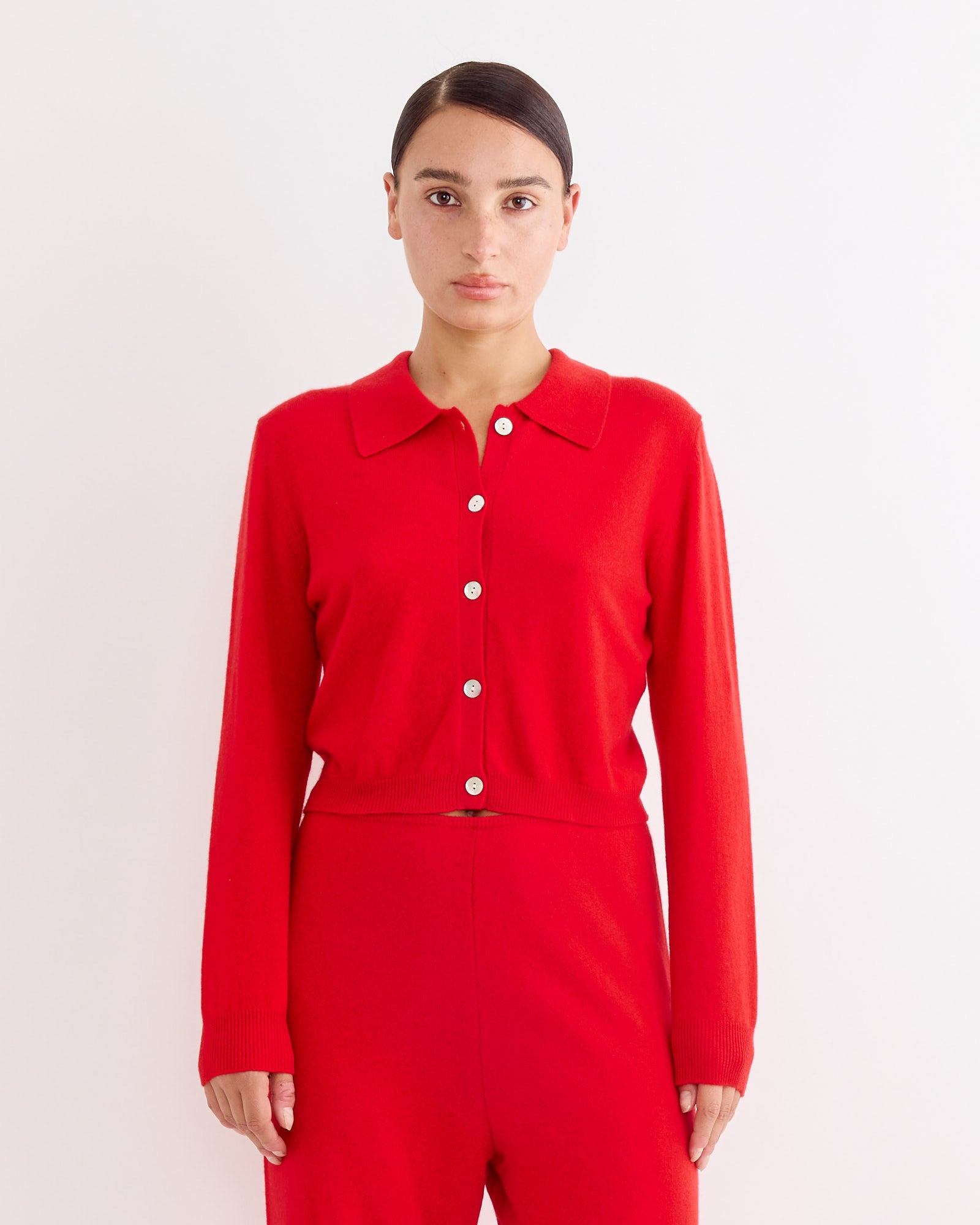 A woman with dark hair pulled back wears the Hai Anselma Cardigan in Red with matching pants, standing against a plain white background.