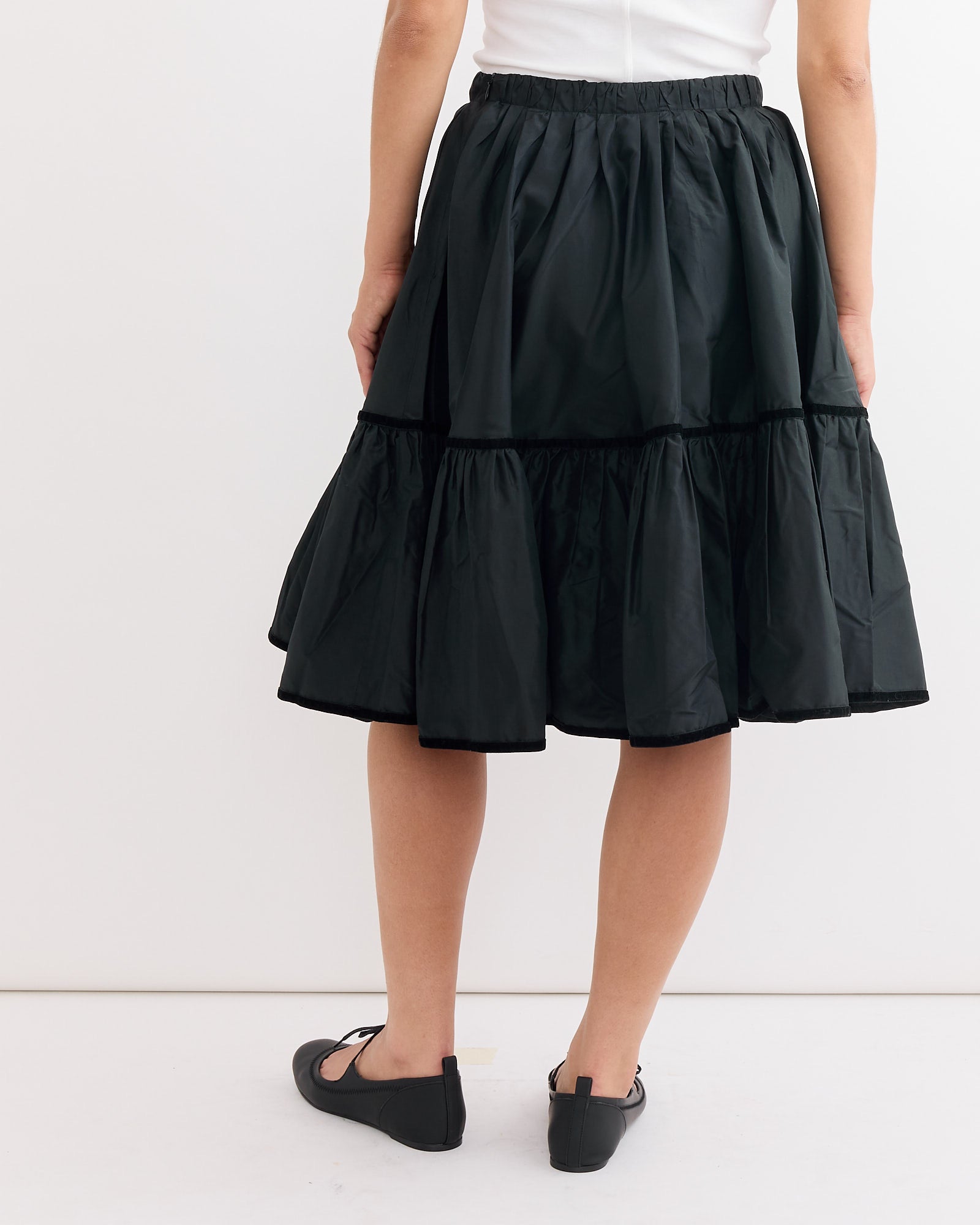 A person is shown from the back wearing a white top, the Hai Ada Skirt in Black (taffeta silk), and black flat shoes, standing against a plain white background.
