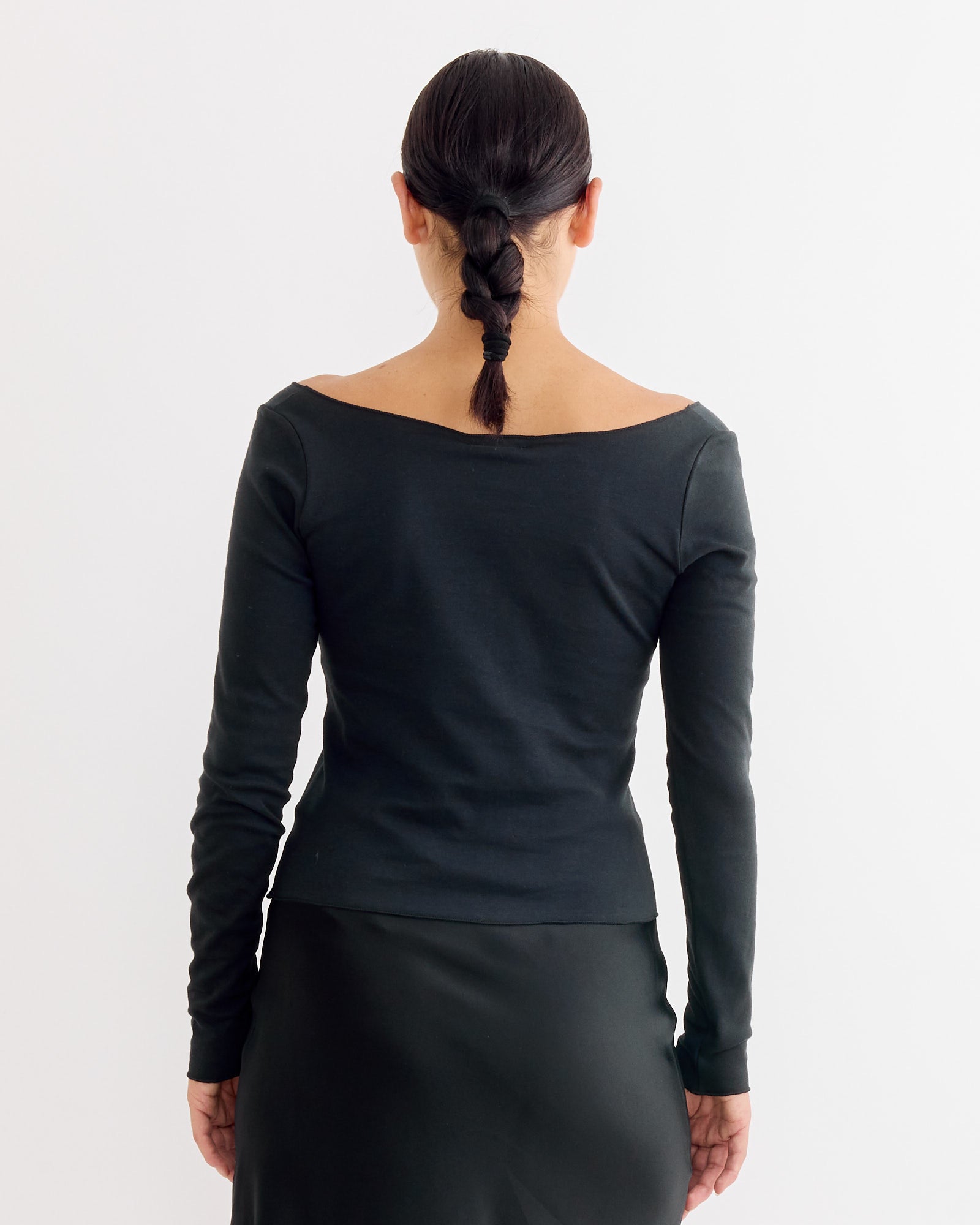 A person with dark braided hair, wearing the Hai Gretchen Tee in Black and a black skirt, stands facing away from the camera against a plain white background.