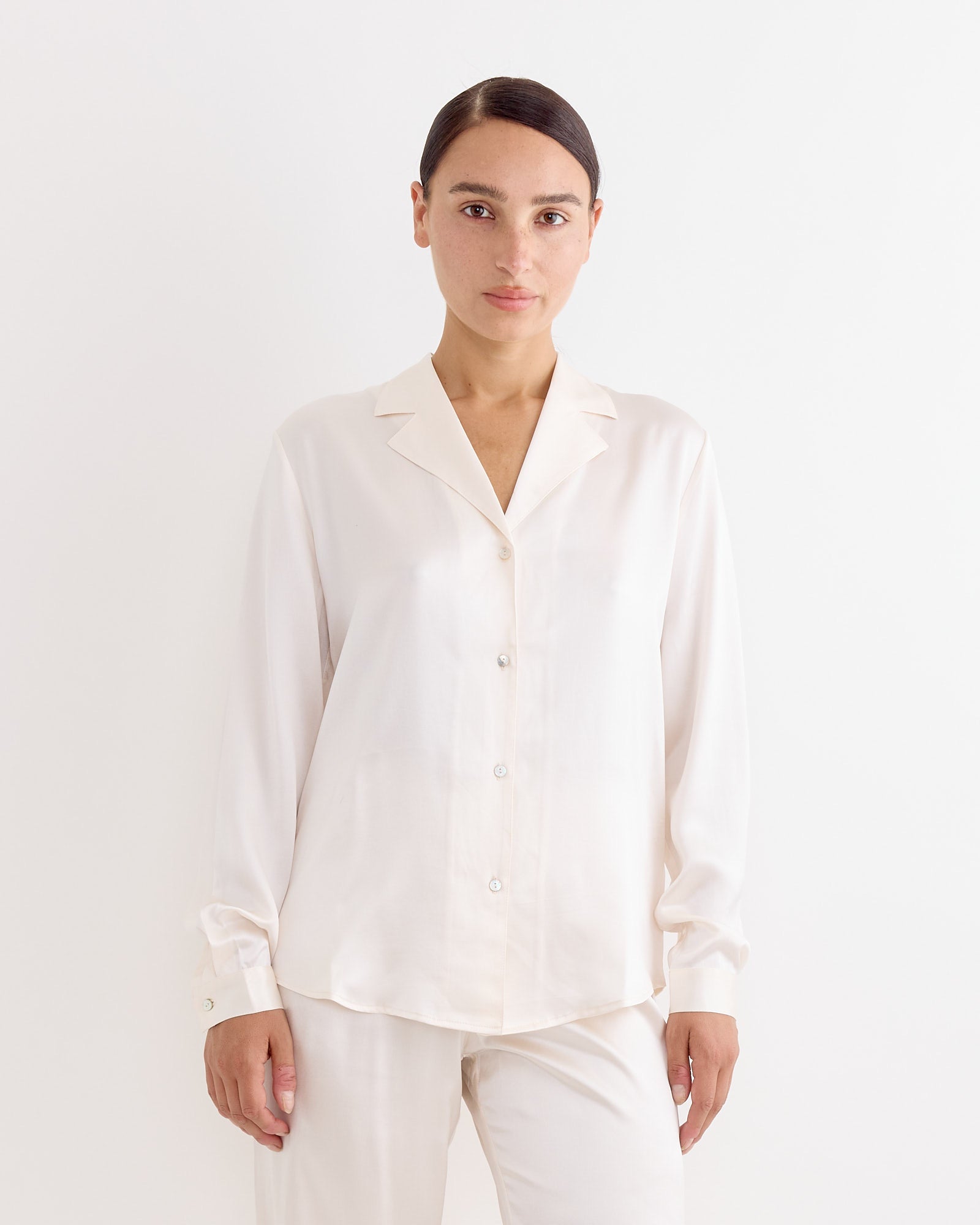 A person with dark hair pulled back is wearing the Hai Irene Blouse in Ivory and matching pants, standing against a plain white background.