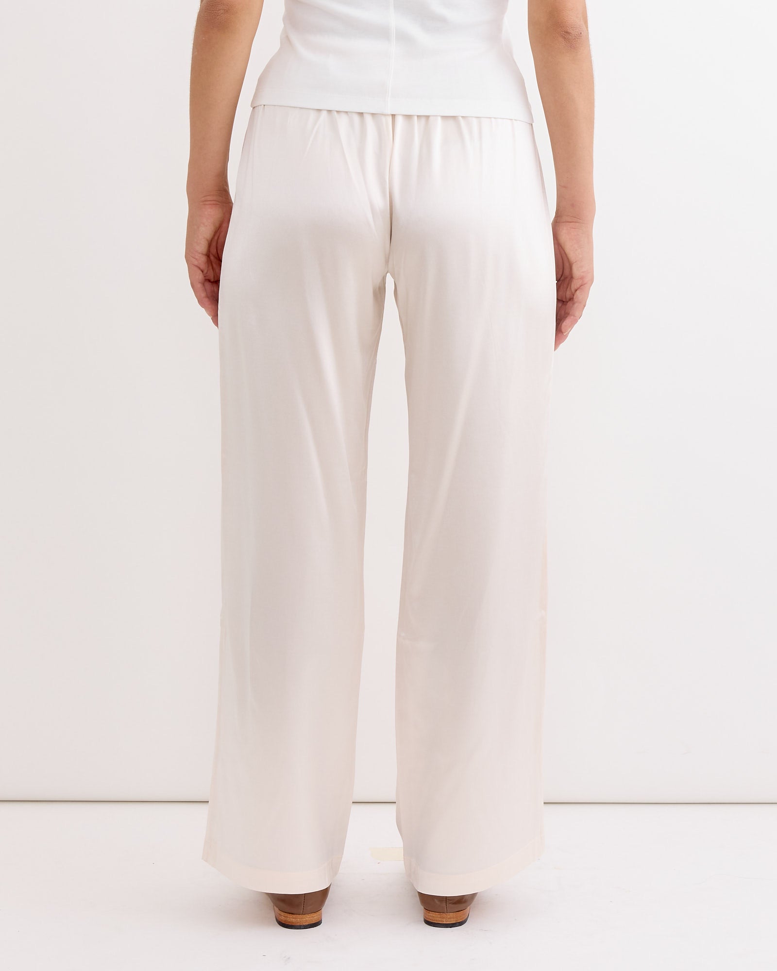 A person stands facing a white wall, shown from the back, wearing Hai's Soma Trouser in Ivory and a white top. Only their lower body is visible.