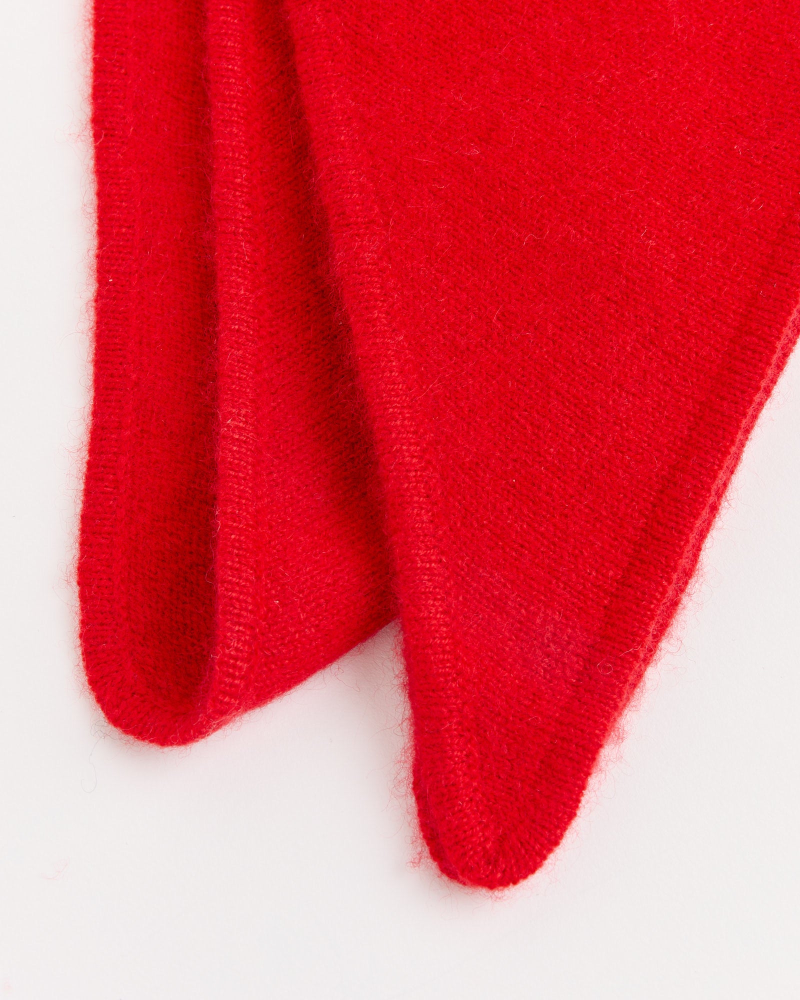 Two overlapping pieces of bright red fabric with pointed tips rest on a white surface. The soft, fuzzy texture suggests they are the Sophia Scarf in Red by Hai, a cozy and stylish accessory.