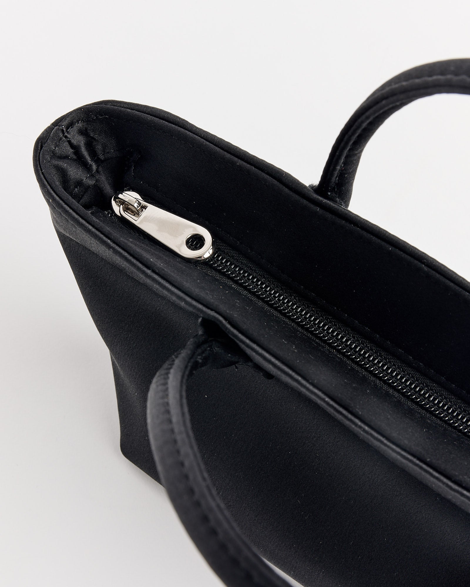 The Otte Bag in Black by Hai is a sleek satin silk bag with a zipper, perfect for adding a stylish touch to any outfit.
