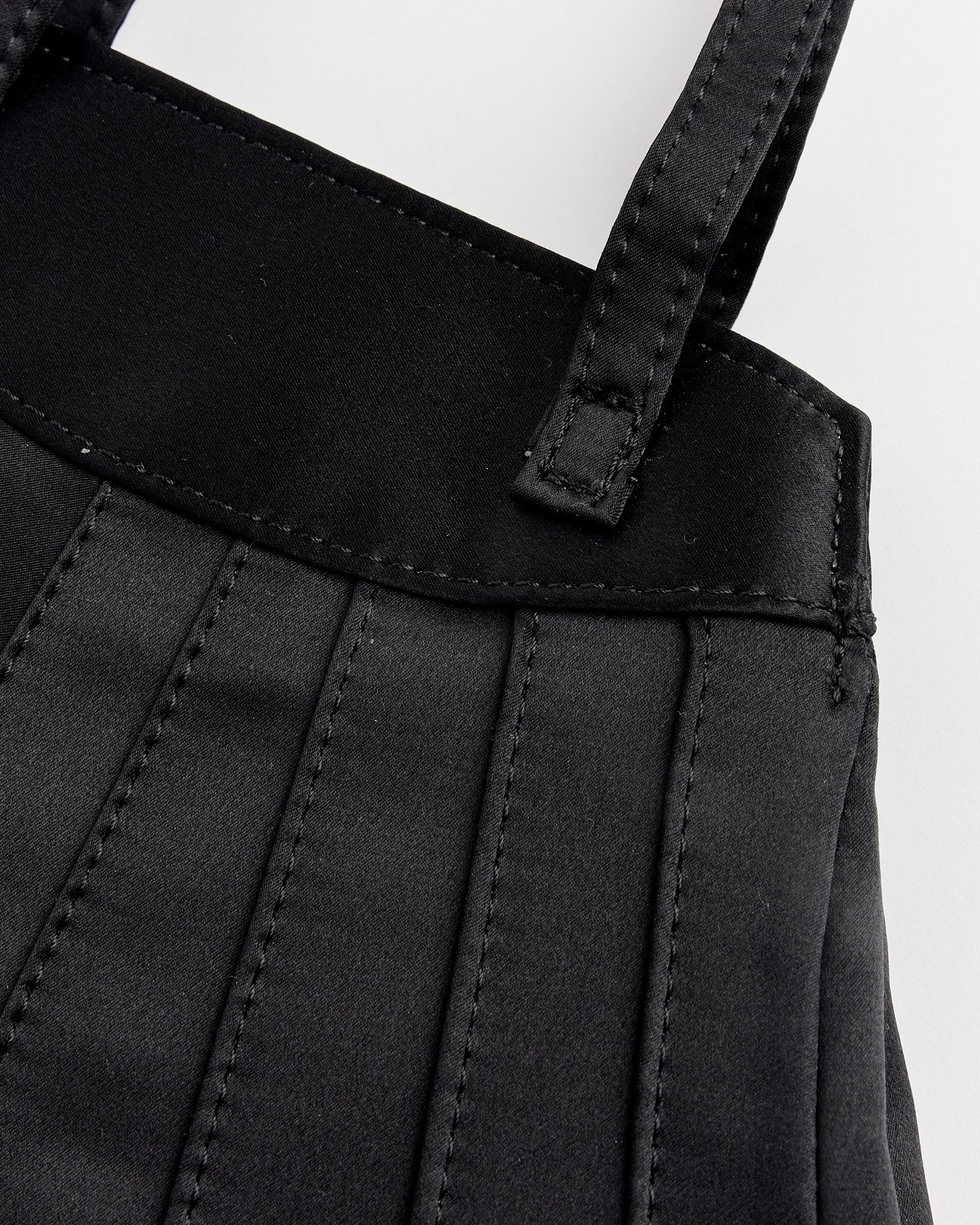 A close-up of a black skirt paired with the Hai Farfalle Bag in Black.