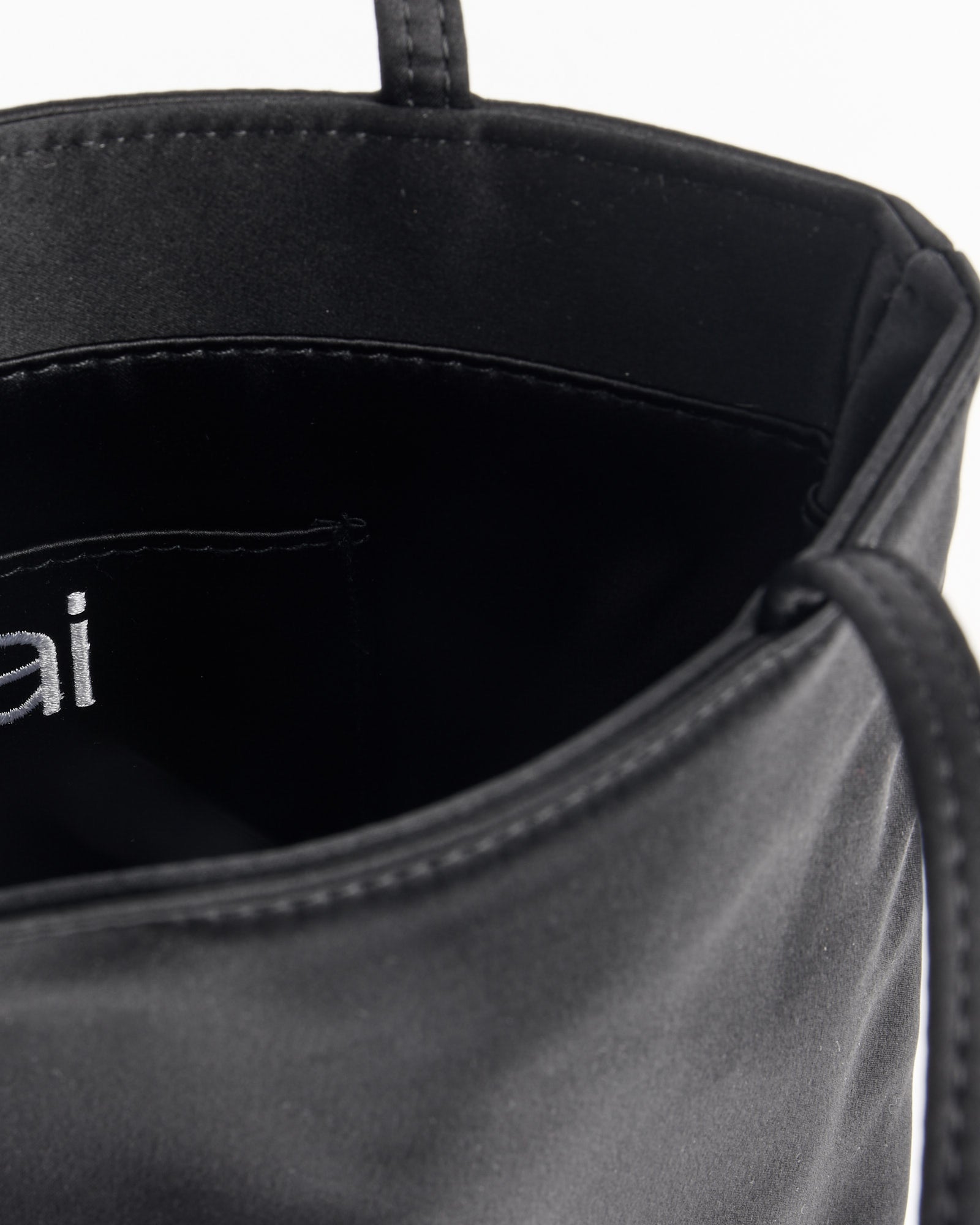 Close-up of the Hai Bobbie Bag in Black, featuring a smooth satin interior with a stitched pocket and part of the white embroidered logo, evoking the luxurious feel of mulberry silk.