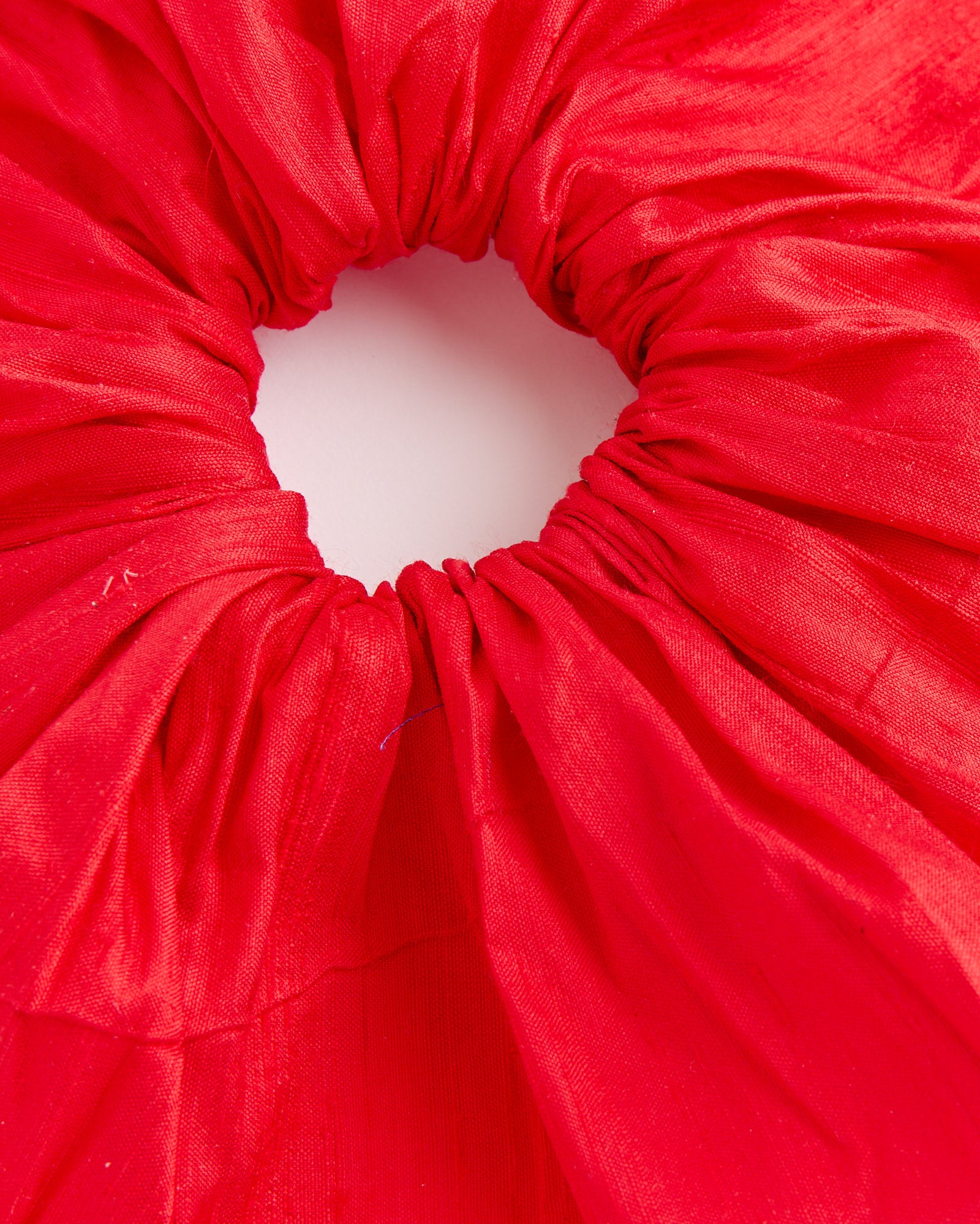 Close-up of a vibrant red Silk Scrunchie by Hai, featuring gathered, ruched Dupion silk texture and arranged in a circle on a white background—a luxurious hair accessory for any occasion.