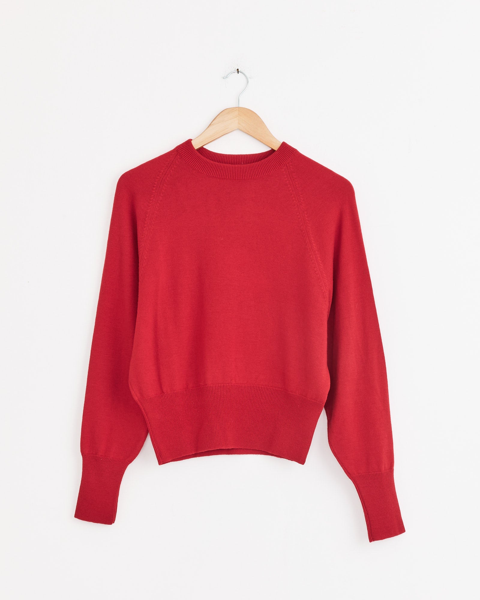 The Cordera Single Wool Sweater in Red, featuring a crew neck and long sleeves, made from extrafine merino wool, hangs on a wooden hanger against a white background.