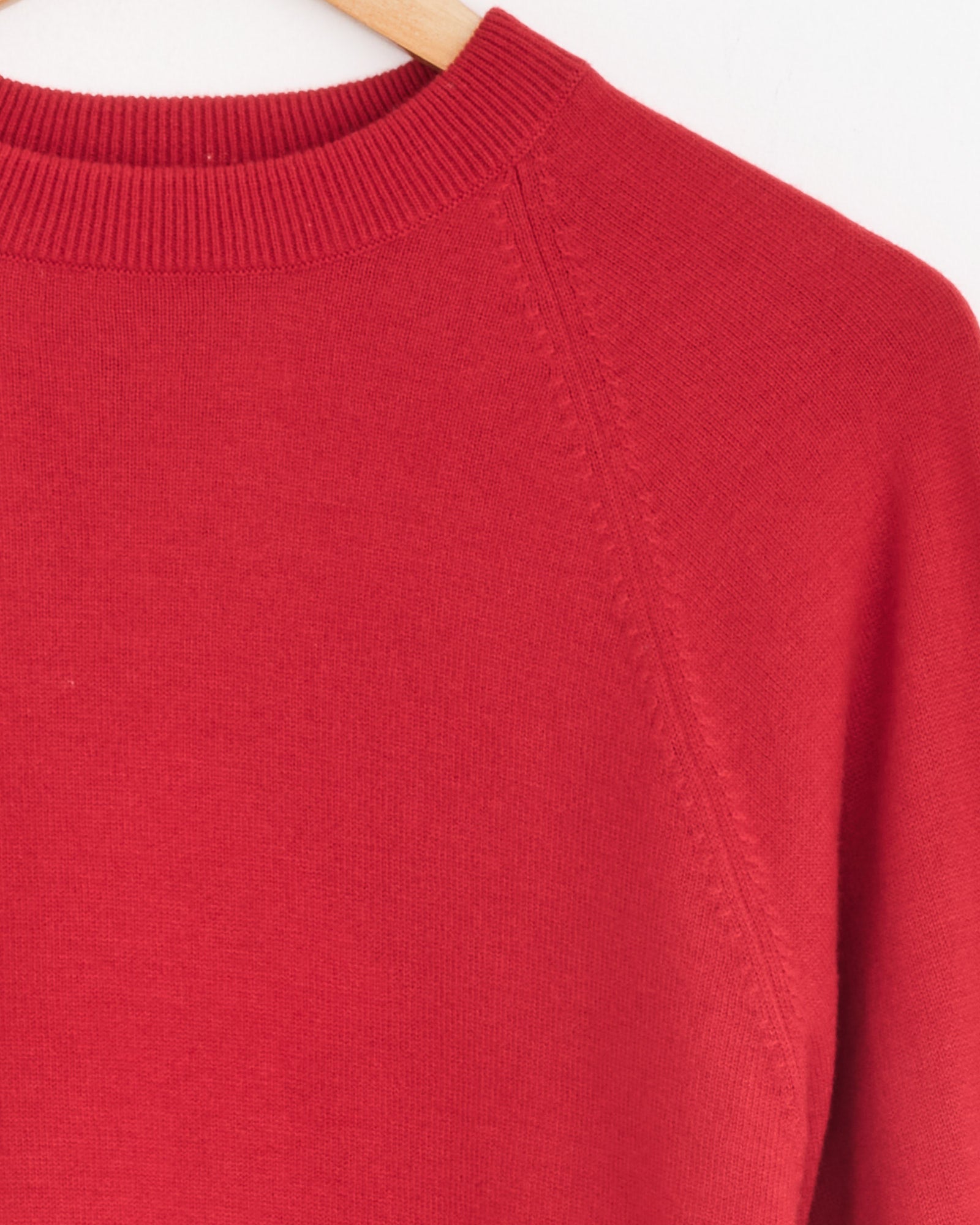 Close-up of the upper section of the Cordera Single Wool Sweater in Red, made from Extrafine Merino Wool, hanging on a wooden hanger and highlighting the round ribbed neckline and shoulder seam detail.