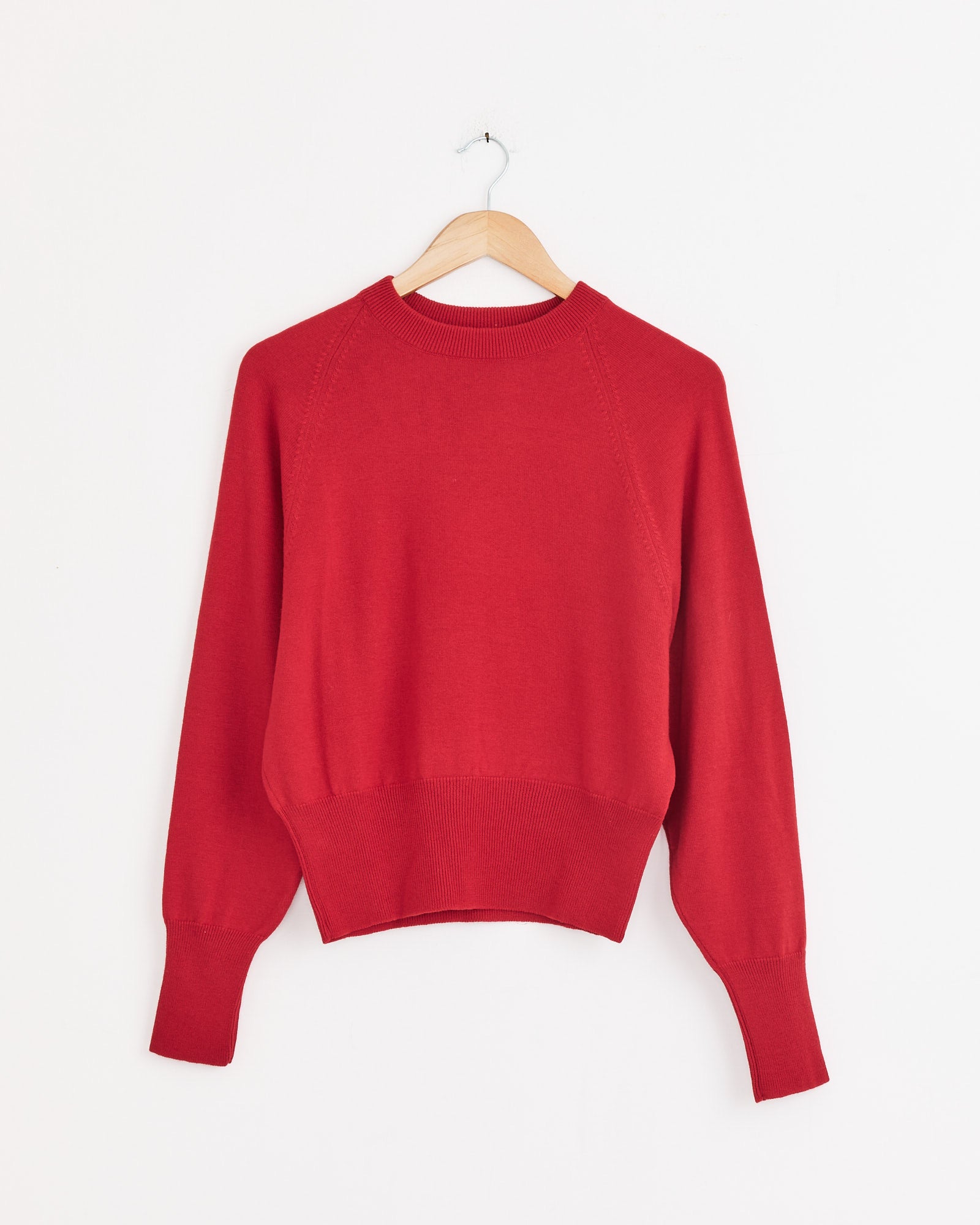 The CORDERA Single Wool Sweater in Red, crafted in Spain from extrafine merino wool with a crew neck, is displayed on a wooden hanger against a plain white background.