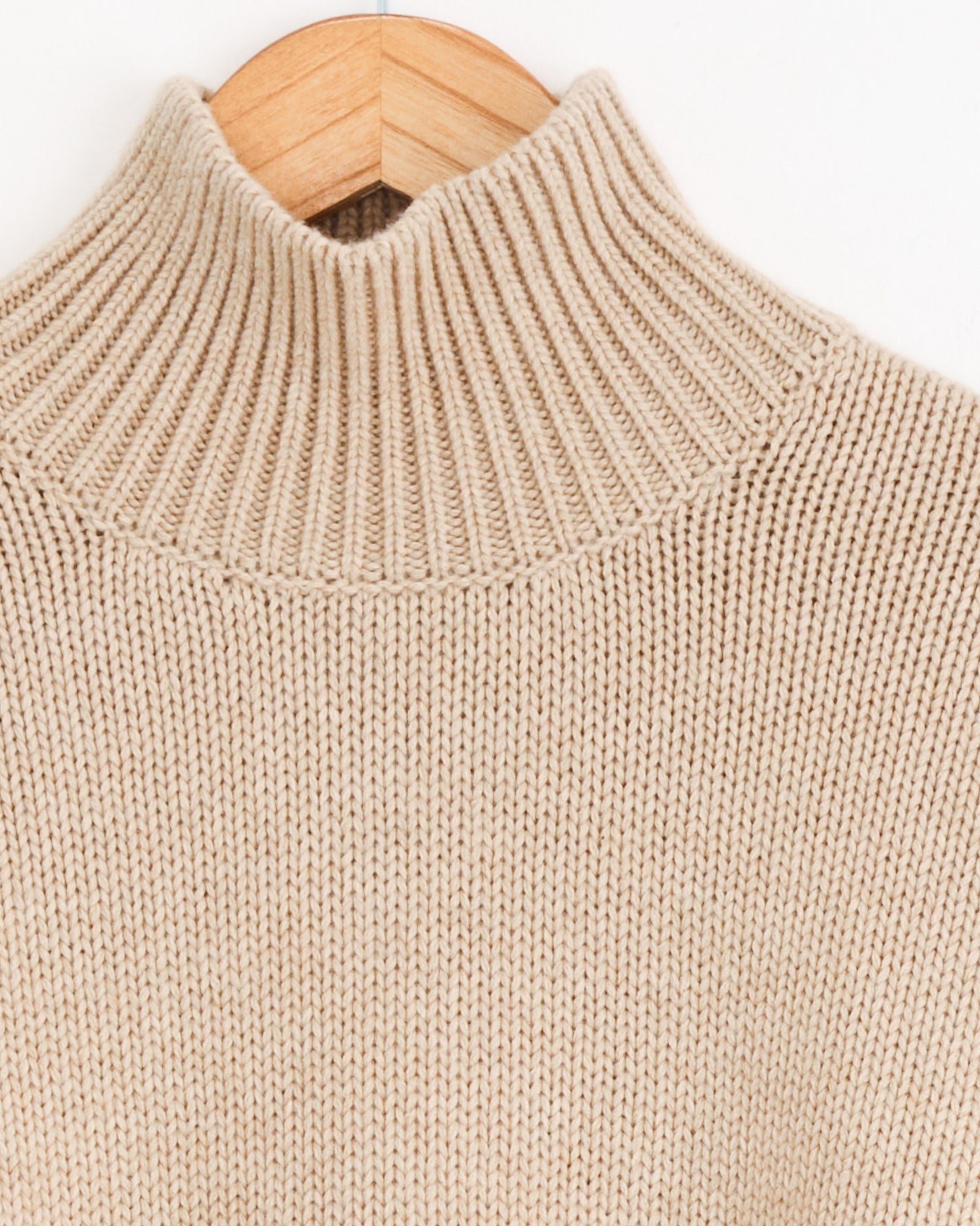Cordera Merino Wool Chunky Turtleneck in Beige—oversized fit with a ribbed texture and turtleneck—displayed from the back on a wooden hanger against a white background.