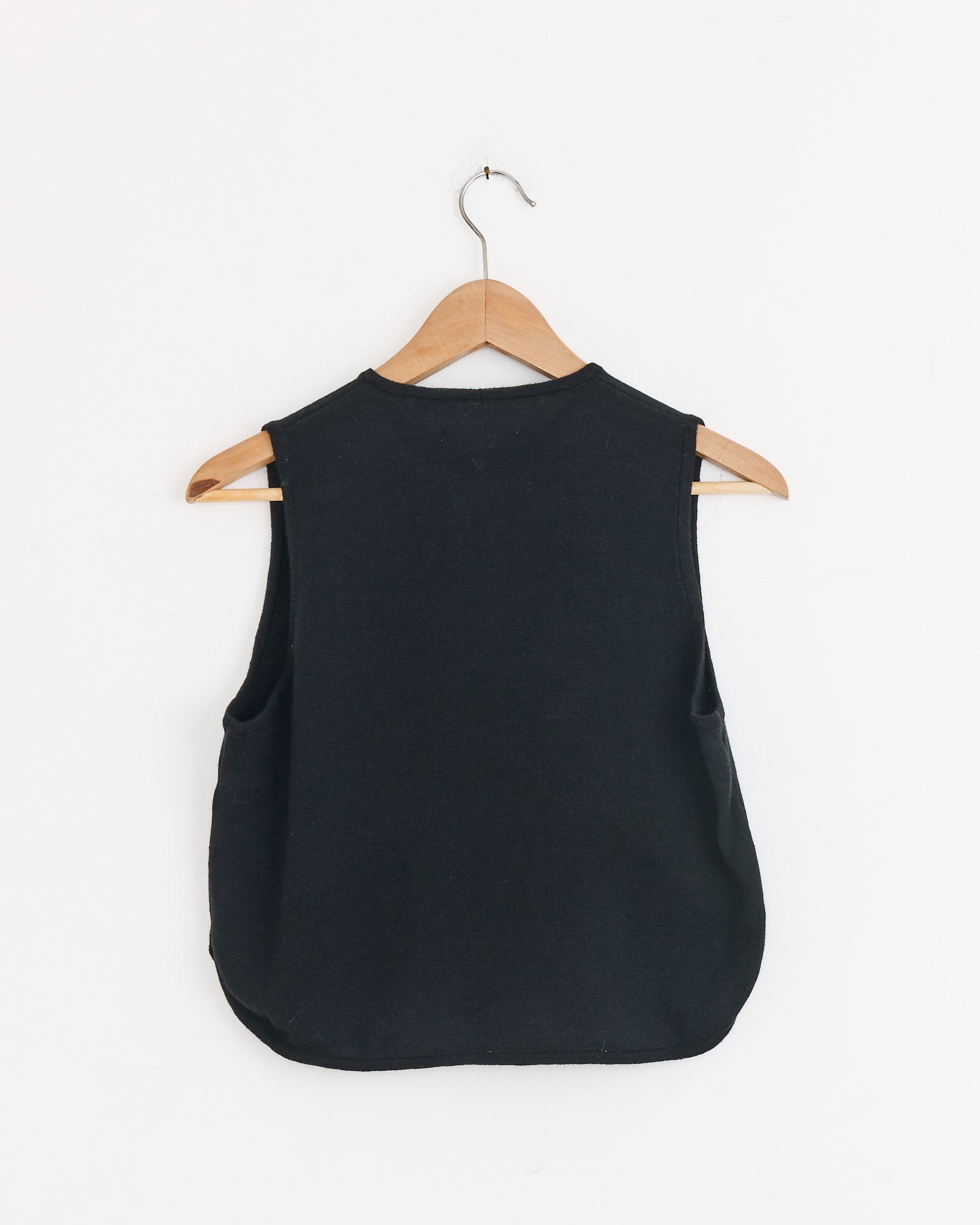 The Merino Wool Waistcoat in Black by CORDERA, crafted ethically in Spain from extrafine merino wool, is displayed from the back on a wooden hanger against a plain white background.