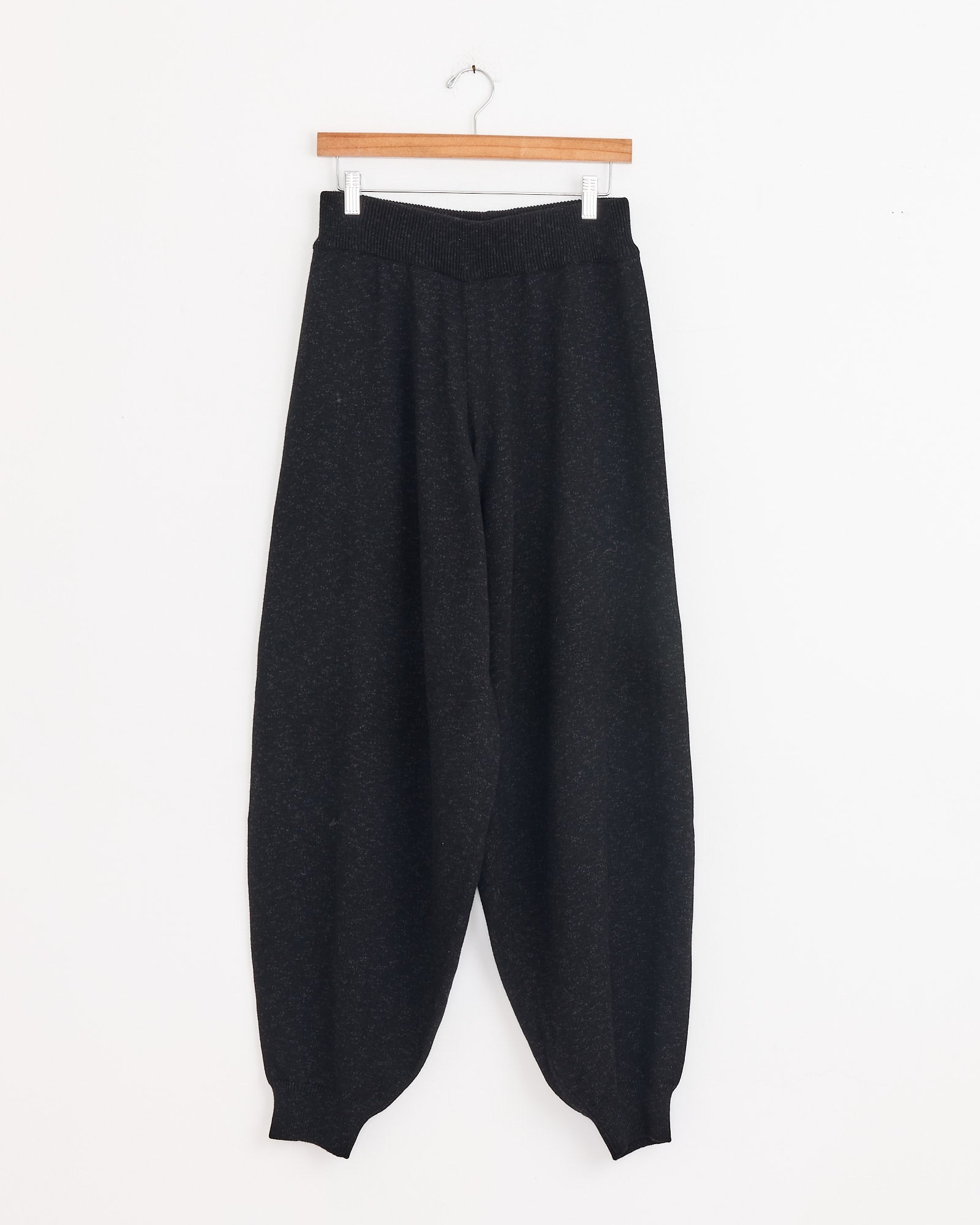 The Cordera Flecked Cotton Pant in Anthracite features a loose fit with an elastic waistband and cuffs, shown hanging on a wooden hanger against a white background for effortless everyday style.