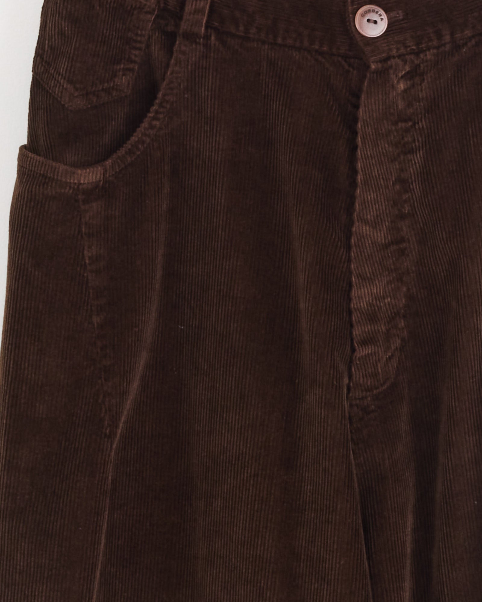 Close-up of Cordera's Baggy Pant in Brown, featuring the waistband, pocket, button, and front seams with visible vertical ridges characteristic of corduroy fabric. Made in Spain.
