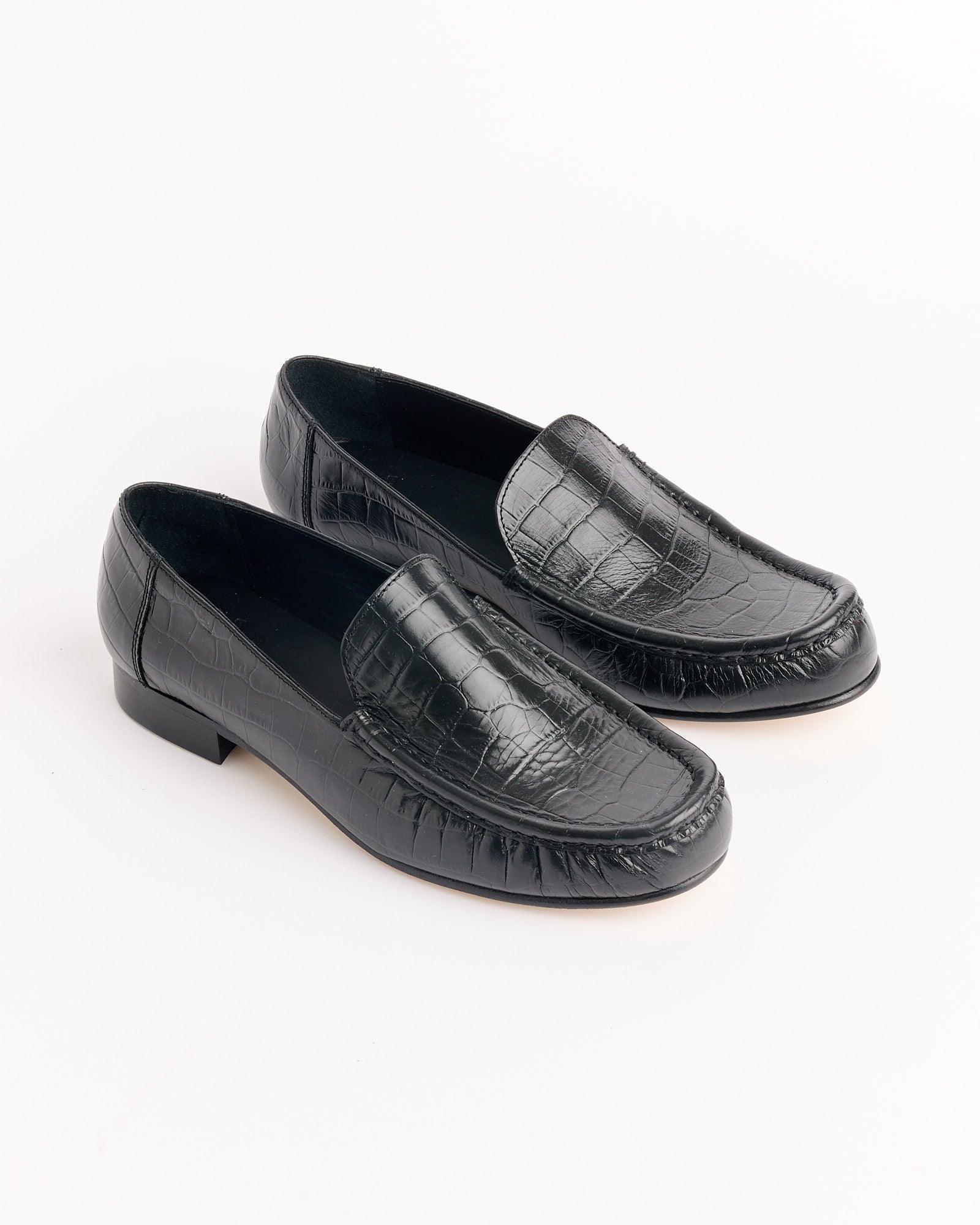 The Cordera Leather Loafer in Black Croco features a crocodile pattern, low heel, and rounded toe, displayed on a white background. Use our online chat for any questions about sizing and fit.