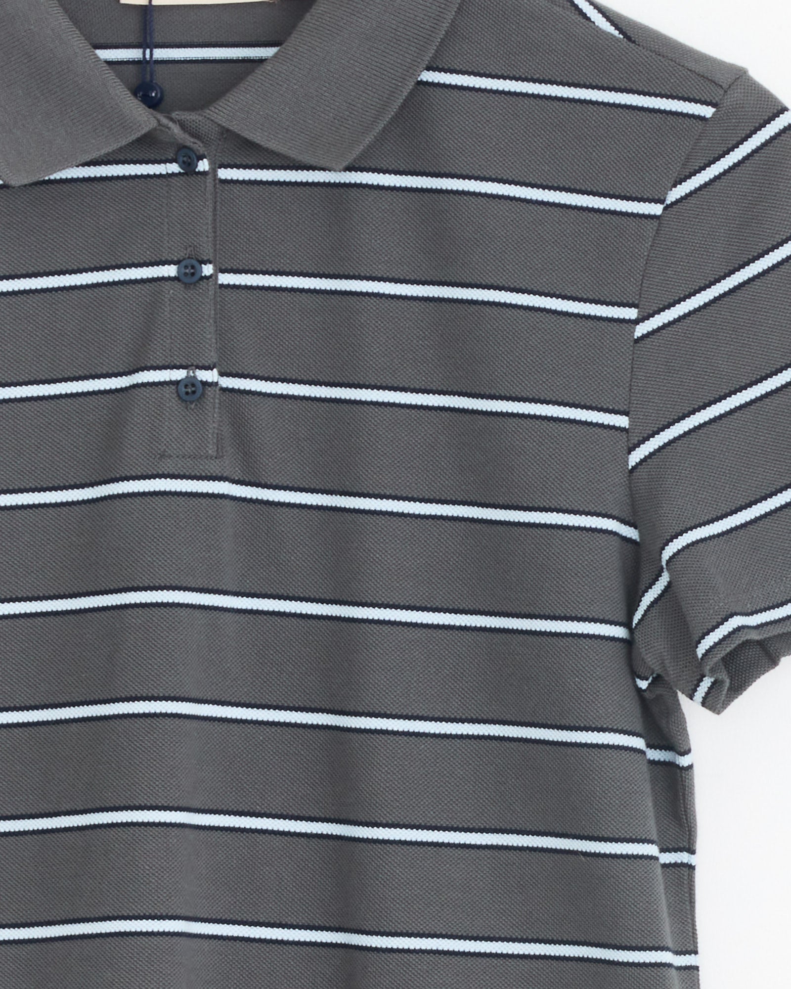 The Julieta Polo in Grey by Paloma Wool is an organic cotton shirt with a collar, short sleeves, and three-button placket. It features thin white and light blue horizontal stripes. Only the upper half of the polo is shown.