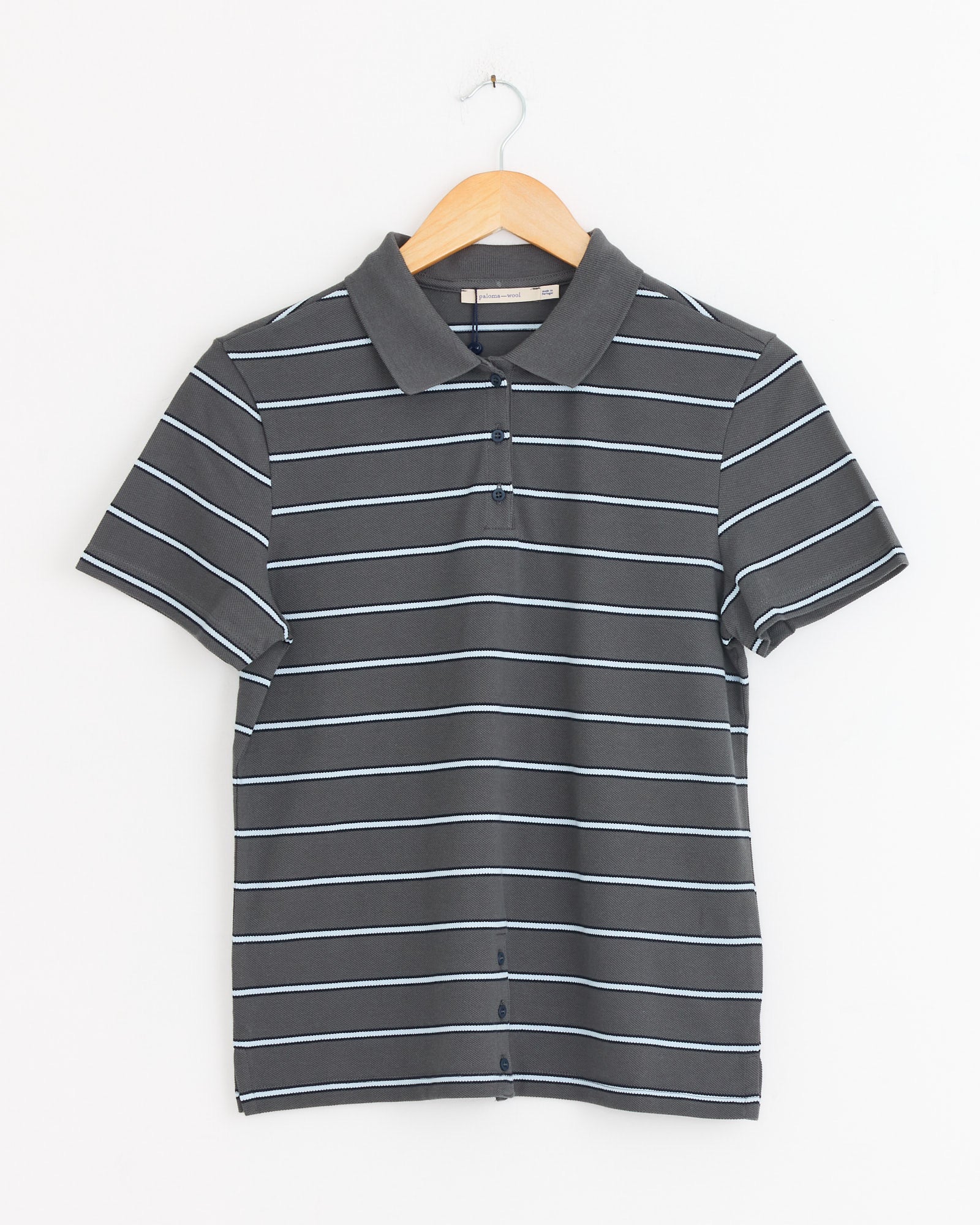 The Paloma Wool Julieta Polo in Grey, a short-sleeved piqué cotton shirt with white stripes, is displayed on a wooden hanger against a plain white background.