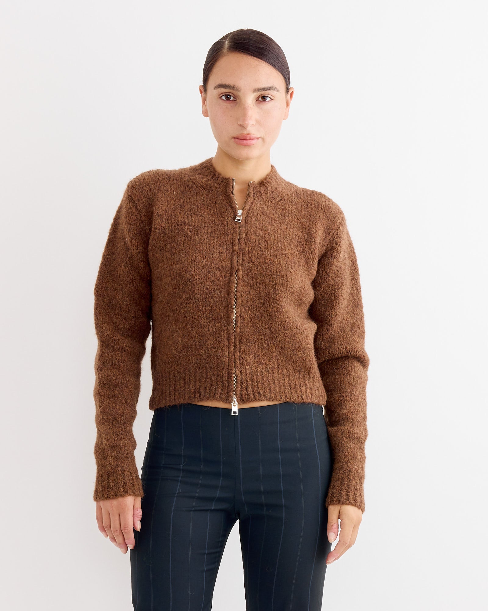 A person wears the Paloma Wool Hasta Luego Zip in Brown, facing forward against a white background to showcase the fit. For sizing help, use our online chat.